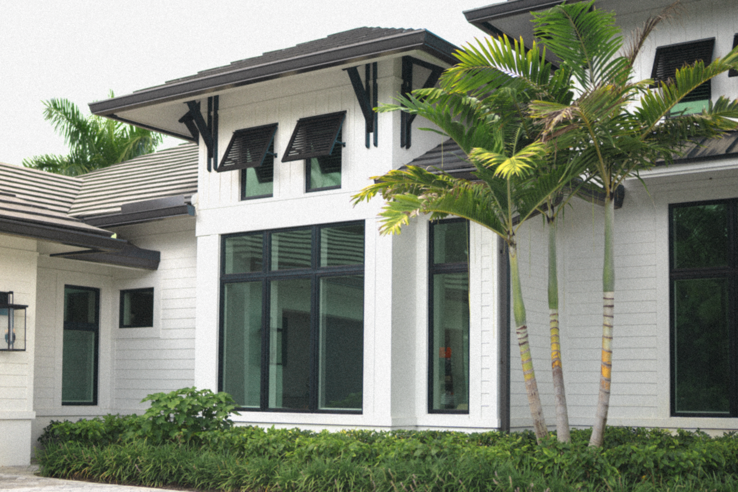 A bedroom with large windows overlooking a river and trees, with a bed in the foreground and a cabinet with decorative vases on top.