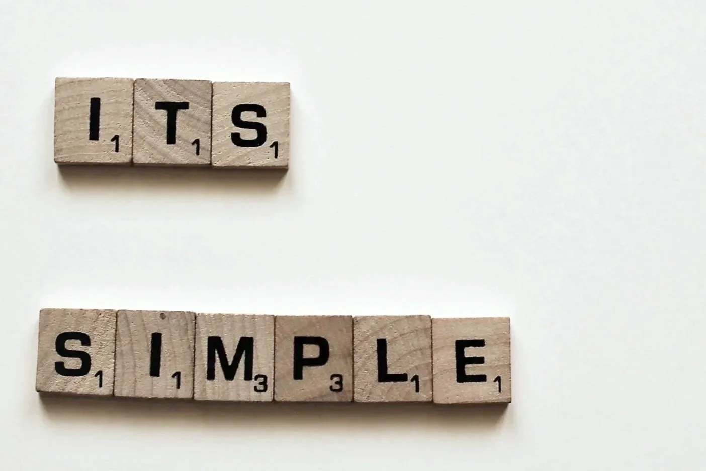 Scrabble tiles spell out the words "ITS" above and "SIMPLE" below on a white surface.
