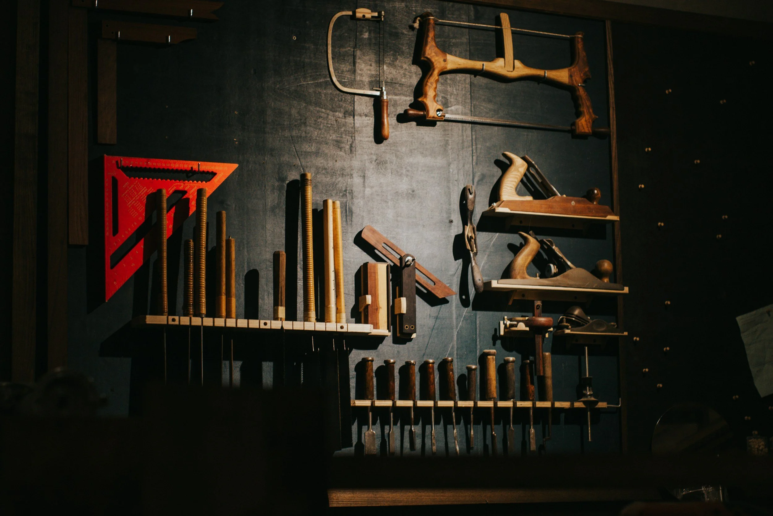 Woodworking hand tools and clamps mounted on a dark wall.