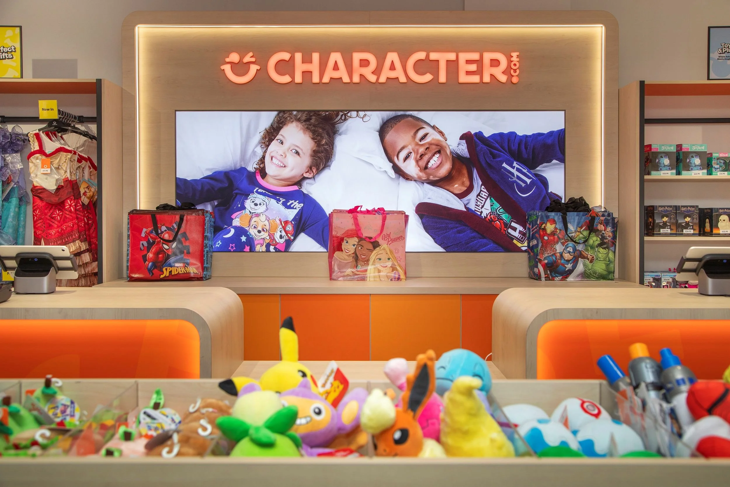 Character.com clothing store sales counter area, with colourful plush toys on display in foreground, a large digital LED lightbox in the background showing two children smiling and Character.com LED illuminated signage.