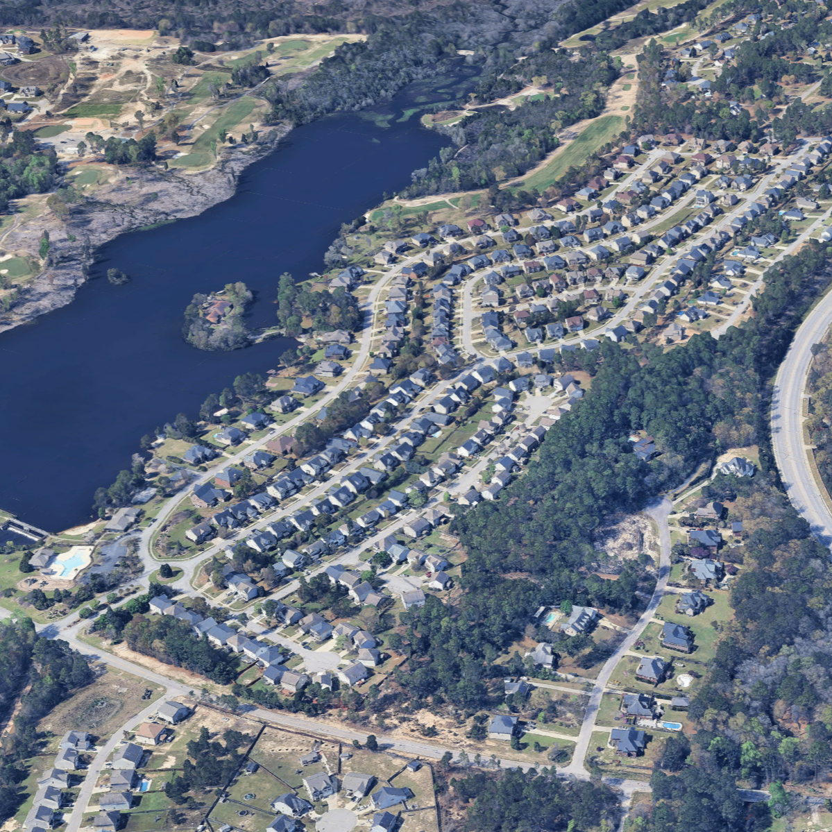 Aerial view of a residential neighborhood next to a large lake, surrounded by trees and green spaces.