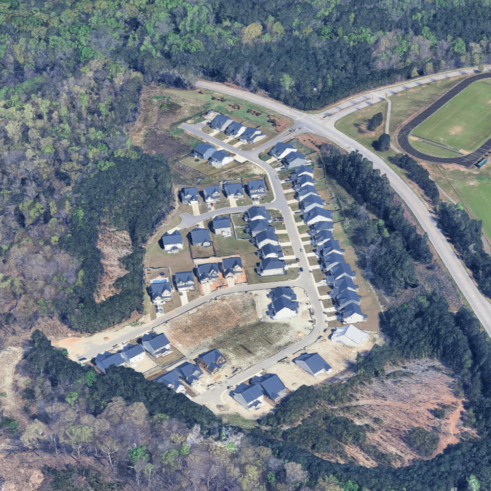 Aerial view of a residential neighborhood surrounded by trees with a sports field and a track nearby.