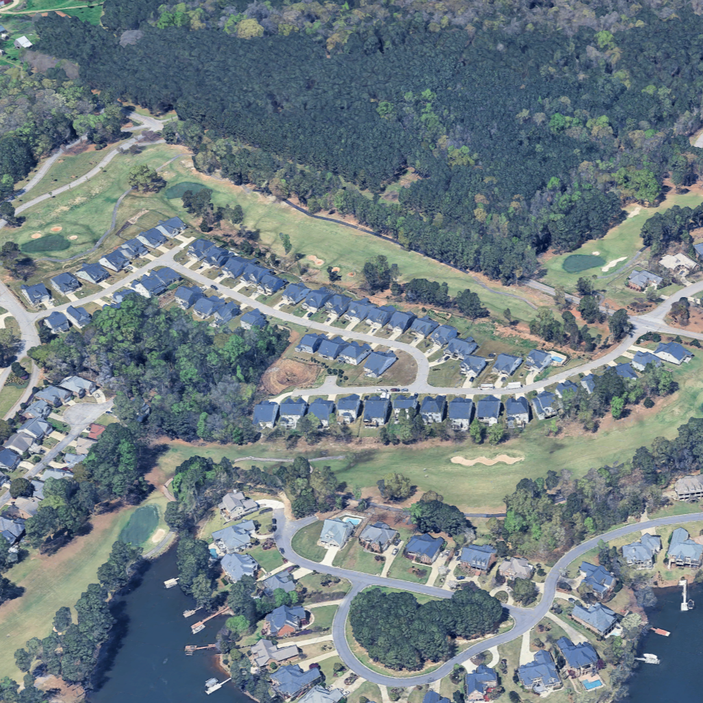 Aerial view of a residential neighborhood with houses, winding roads, golf course, and a wooded area with trees.