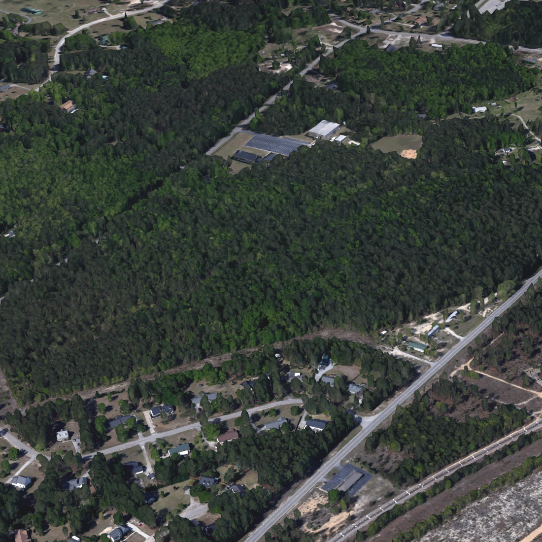 Aerial view of a residential neighborhood with houses, roads, and a large area of dense green trees and forest.