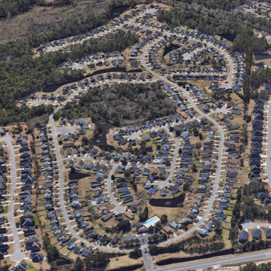 Aerial view of a suburban neighborhood with winding roads, houses, small lakes, and a swimming pool, surrounded by trees.
