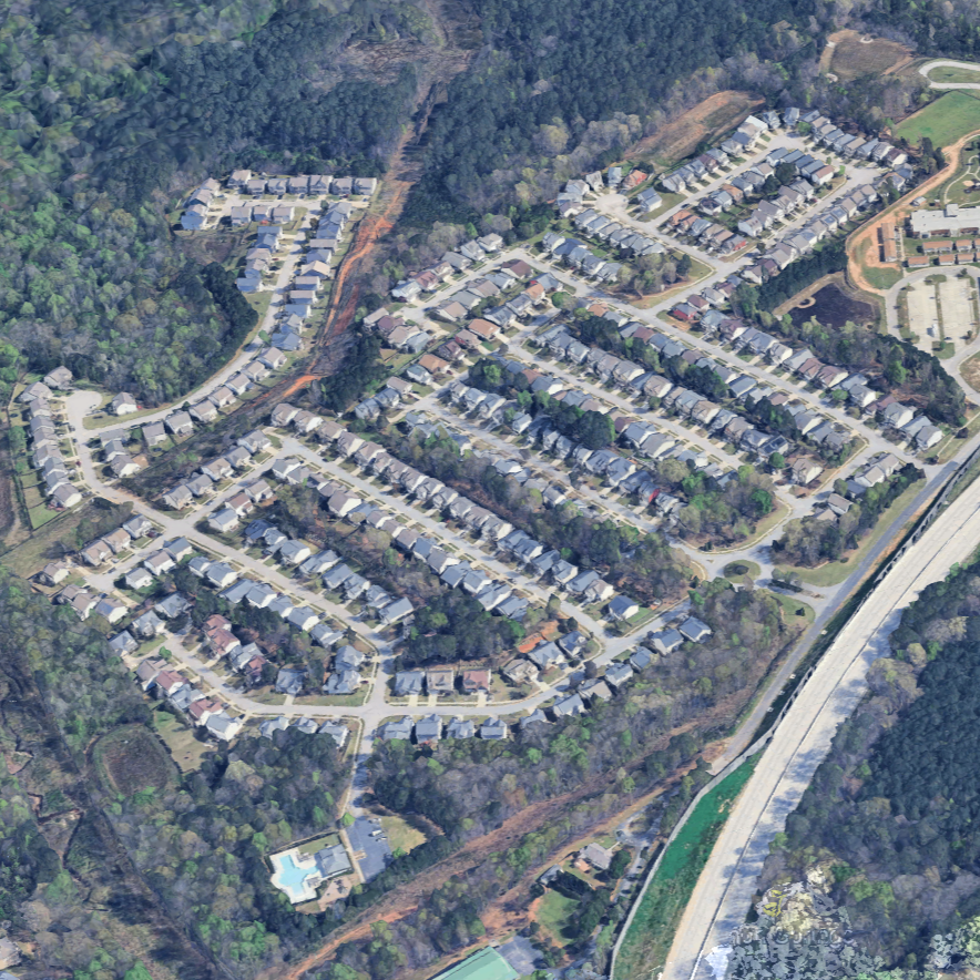Aerial view of a residential neighborhood with houses, streets, a swimming pool, and surrounding wooded areas.