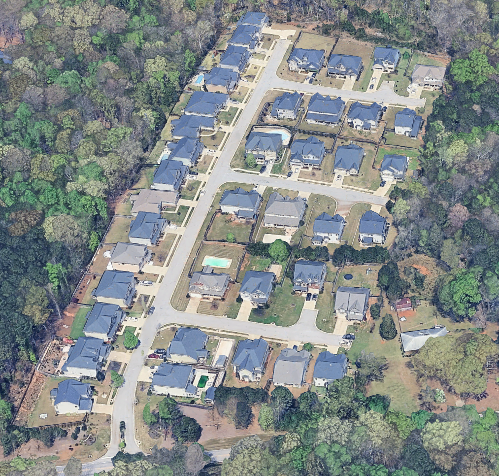 Aerial view of a suburban residential neighborhood with houses, streets, and surrounding trees.