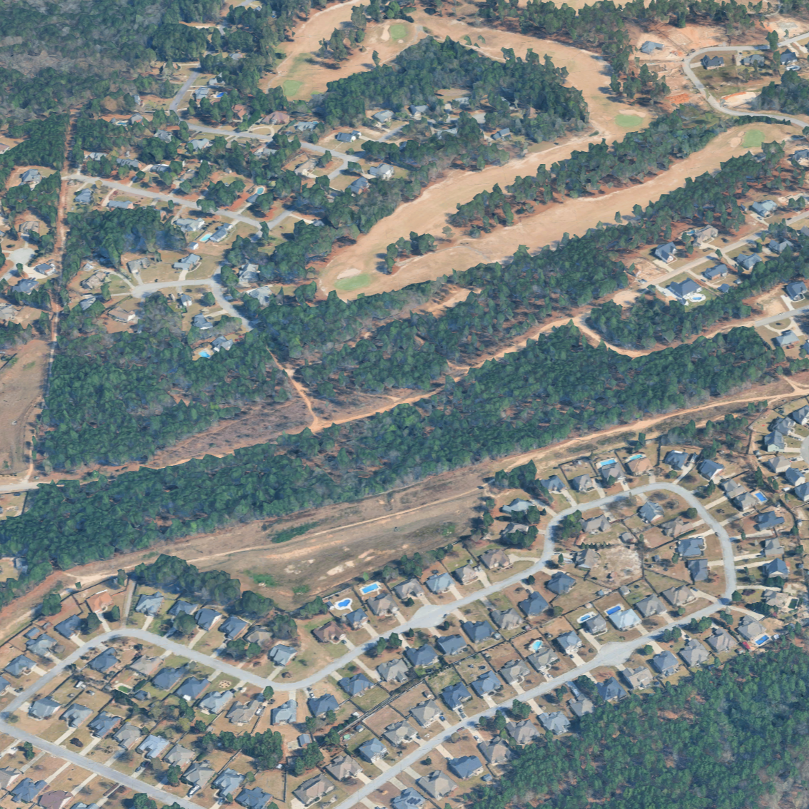 Aerial view of a suburban neighborhood with winding roads, houses, and a large wooded area with some cleared land.
