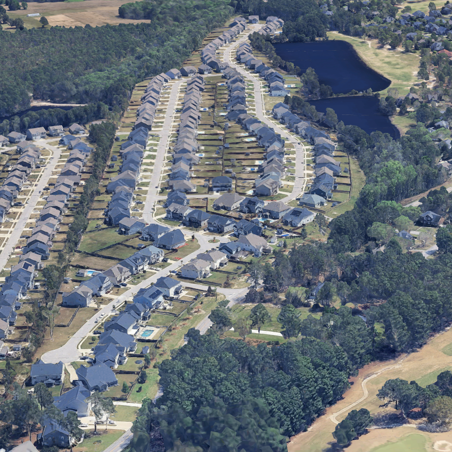 Aerial view of a suburban neighborhood with rows of houses, green lawns, and a couple of ponds surrounded by trees.