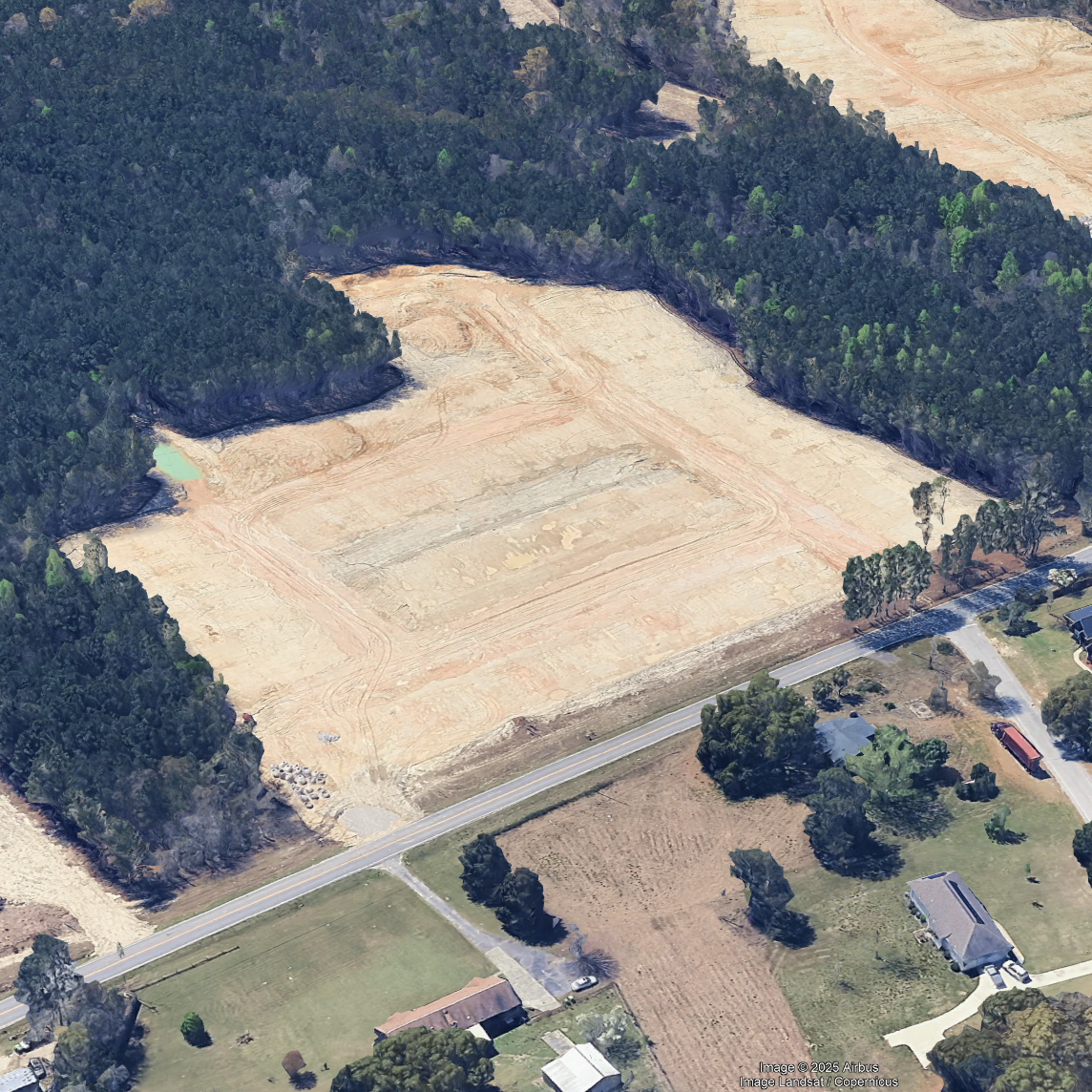 Aerial view of a construction site with cleared land and surrounding trees in a residential area.