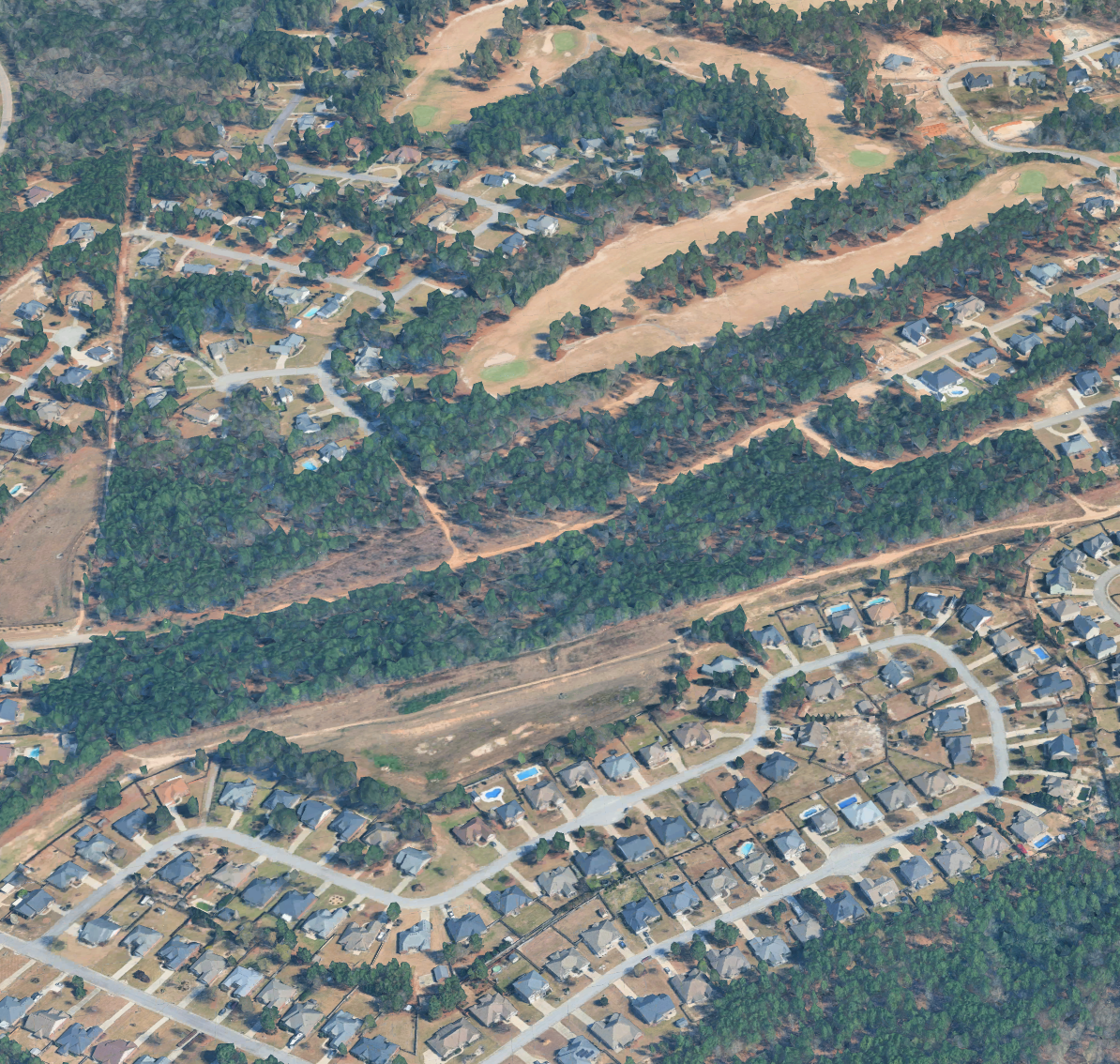 Aerial view of a suburban neighborhood with houses, roads, and a wooded area.