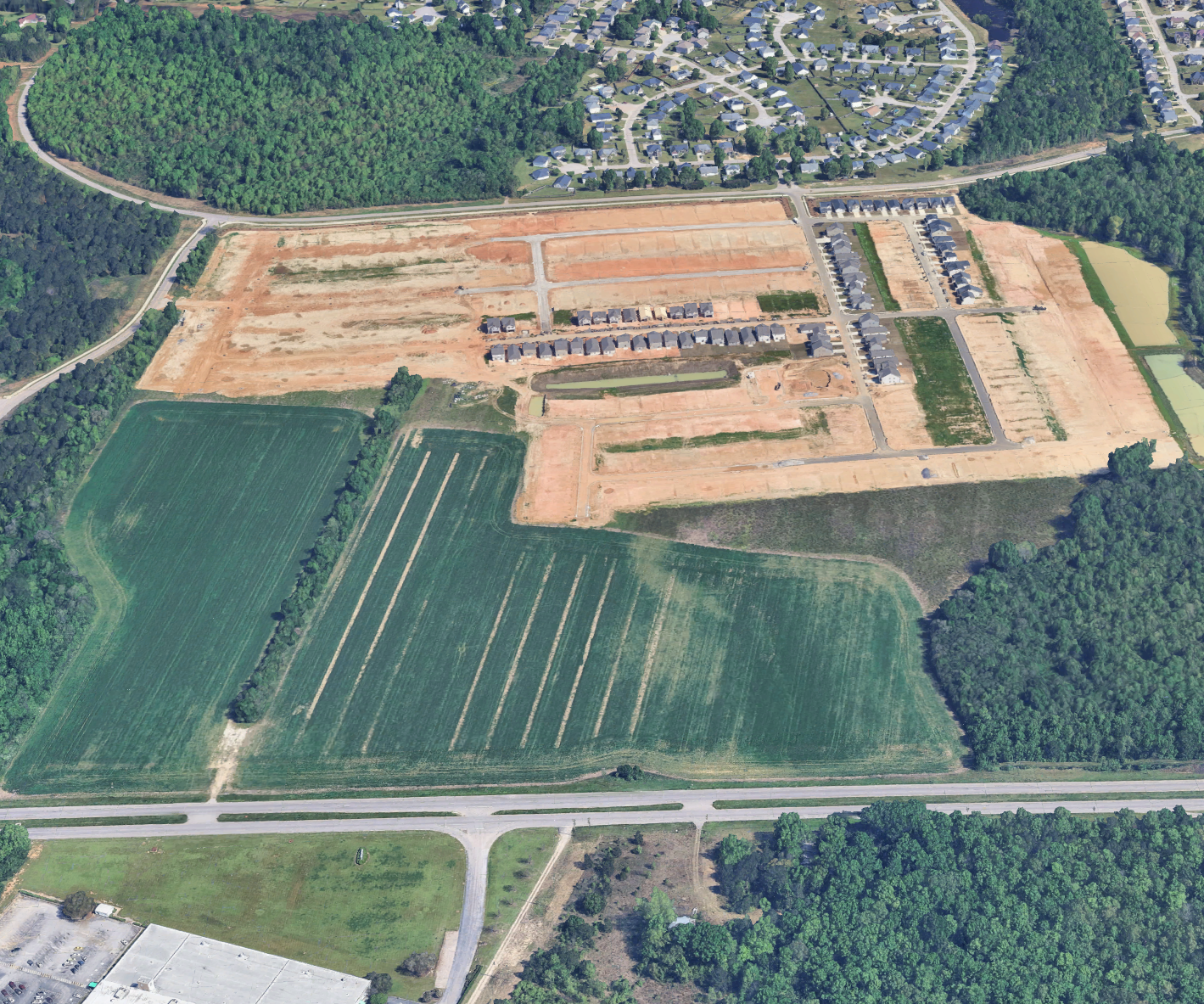 Aerial view of a residential area under construction with houses, roads, and green fields.