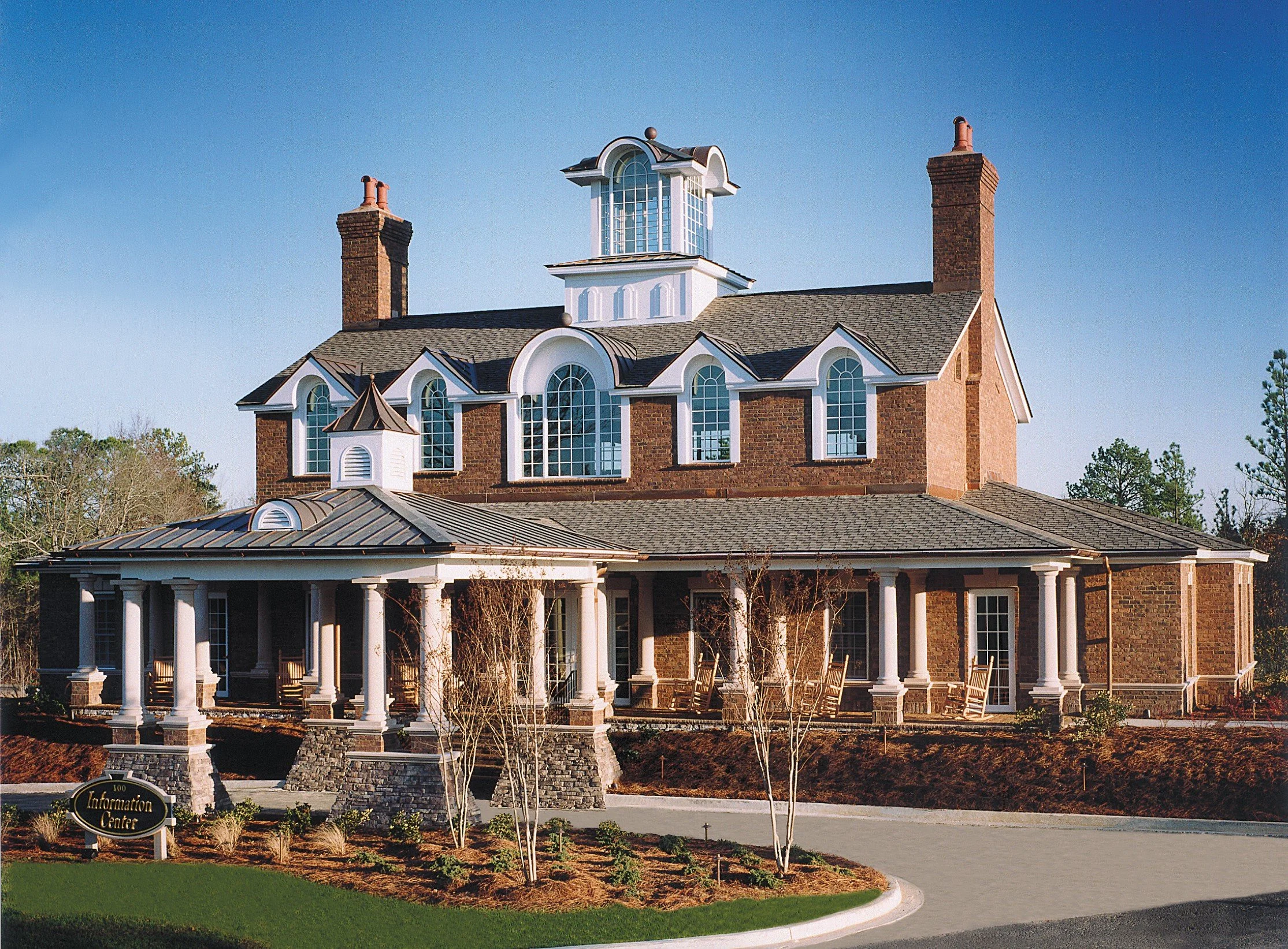 Large brick building with white columns and numerous arched windows, topped with two brick chimneys, and a small decorative turret at the front, surrounded by landscaped grounds.