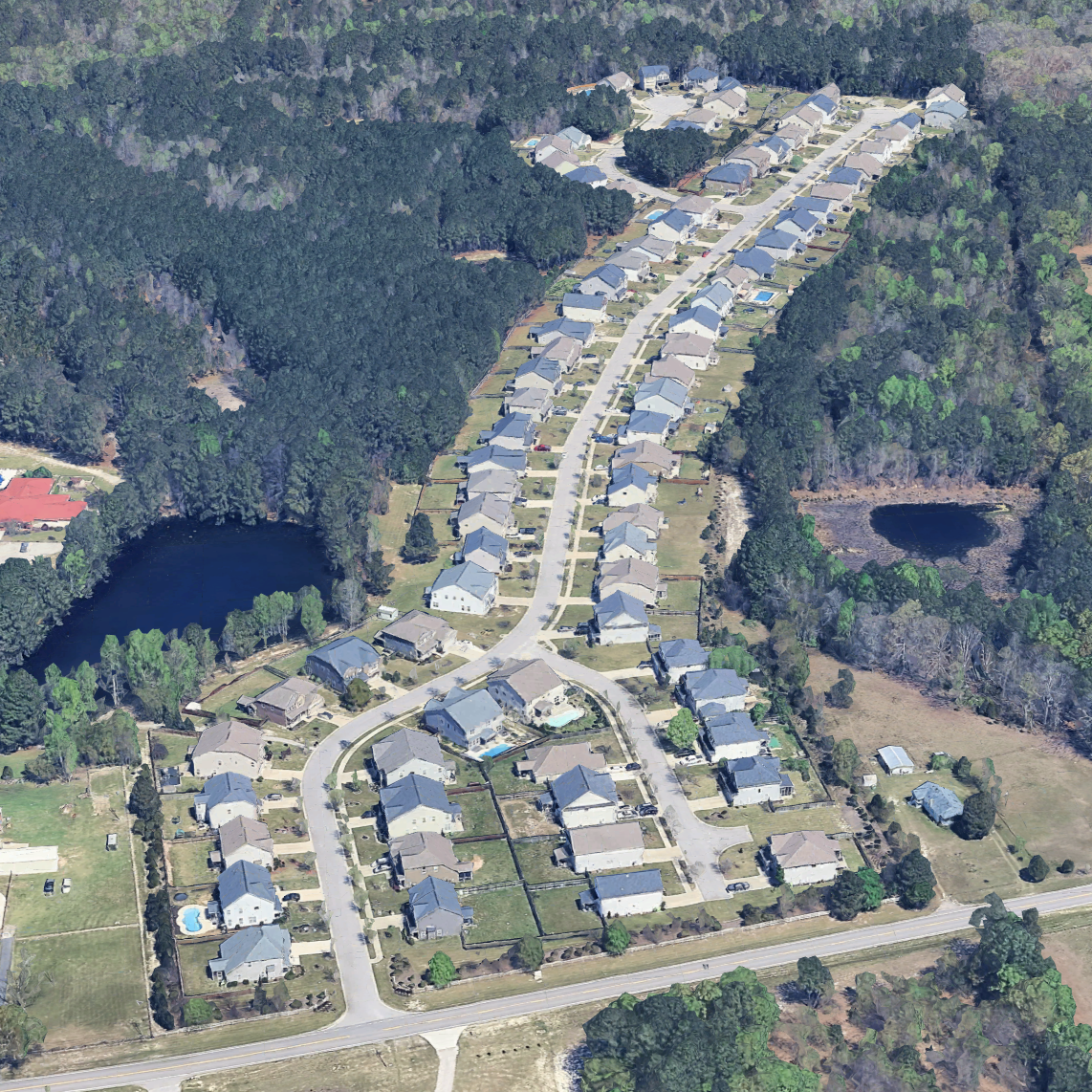 Aerial view of a suburban neighborhood with houses, a winding street, a pond, and wooded areas.