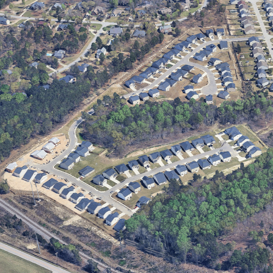 Aerial view of a residential neighborhood with houses, tree-lined areas, and winding streets.