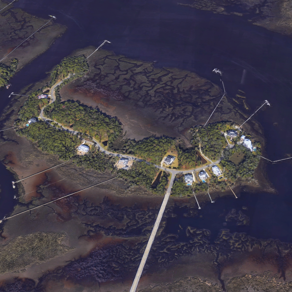 Aerial view of a small island with houses, surrounded by water and marshland, connected to the mainland by a long bridge.