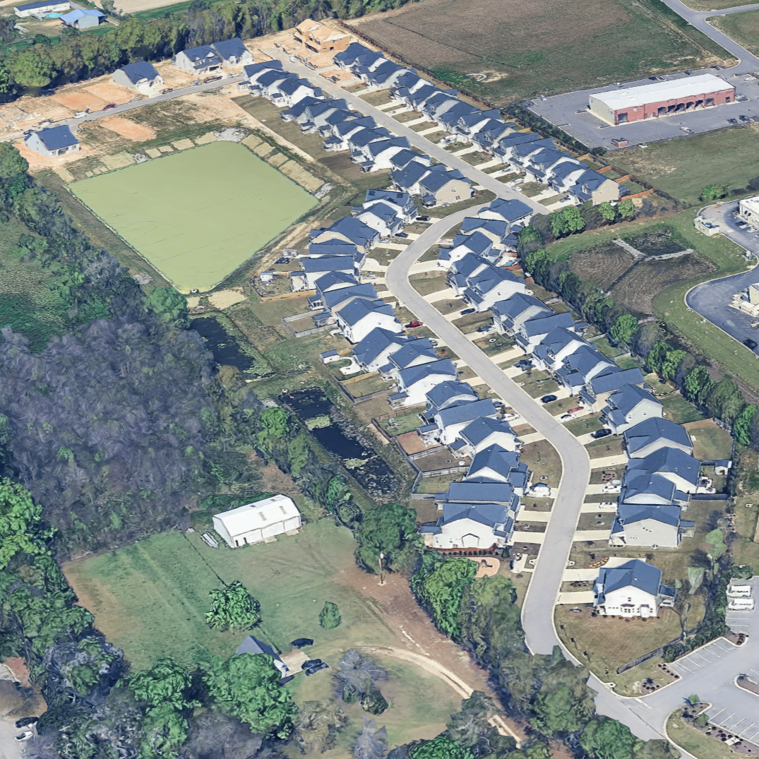 Aerial view of a residential neighborhood with houses, a pond, and surrounding greenery.
