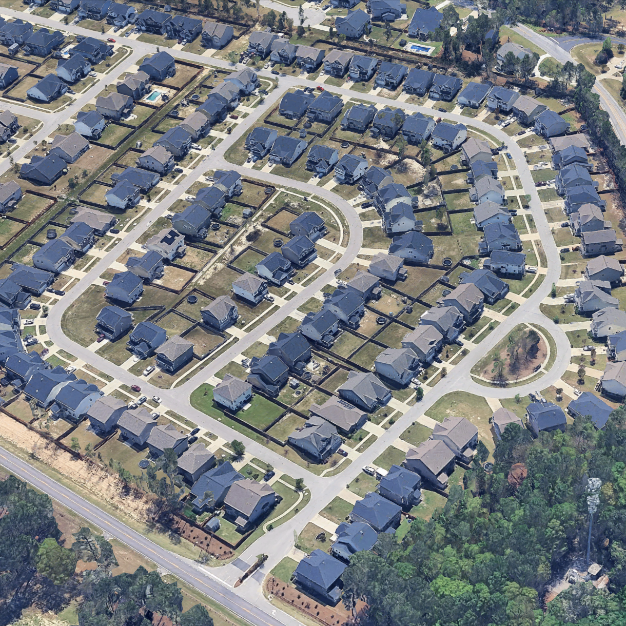 An aerial view of a suburban neighborhood featuring several houses with yards, curving streets, and some trees.
