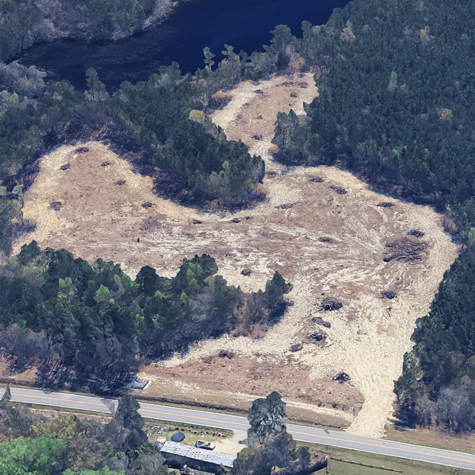 Aerial view of a cleared patch of land surrounded by dense forest next to a road.