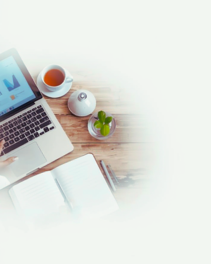 A workspace with a laptop displaying a graph, a cup of tea, a small potted plant, an open notebook, and a pen on a wooden table.