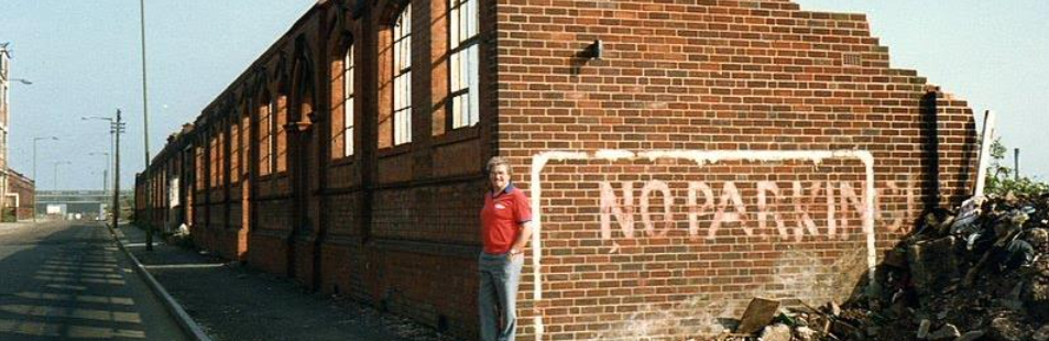 A man standing next to a brick wall with a stencil reading 'NO PARKING' and a pile of debris nearby.