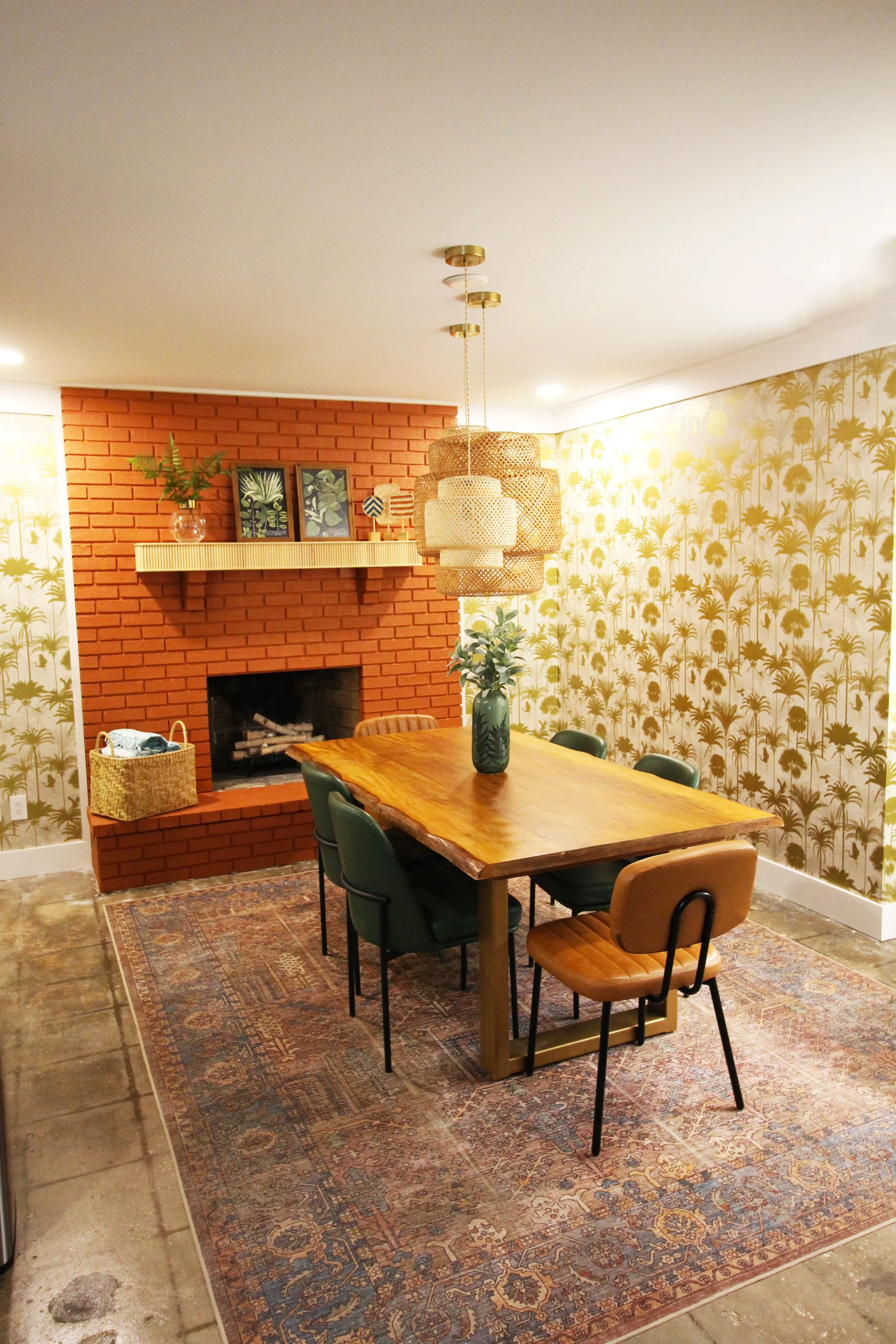 A dining room with a live-edge wood table, six stylish leather chairs, a painted brick fireplace, and tropical-themed wallpaper, illuminated by layered boho style hanging lights.