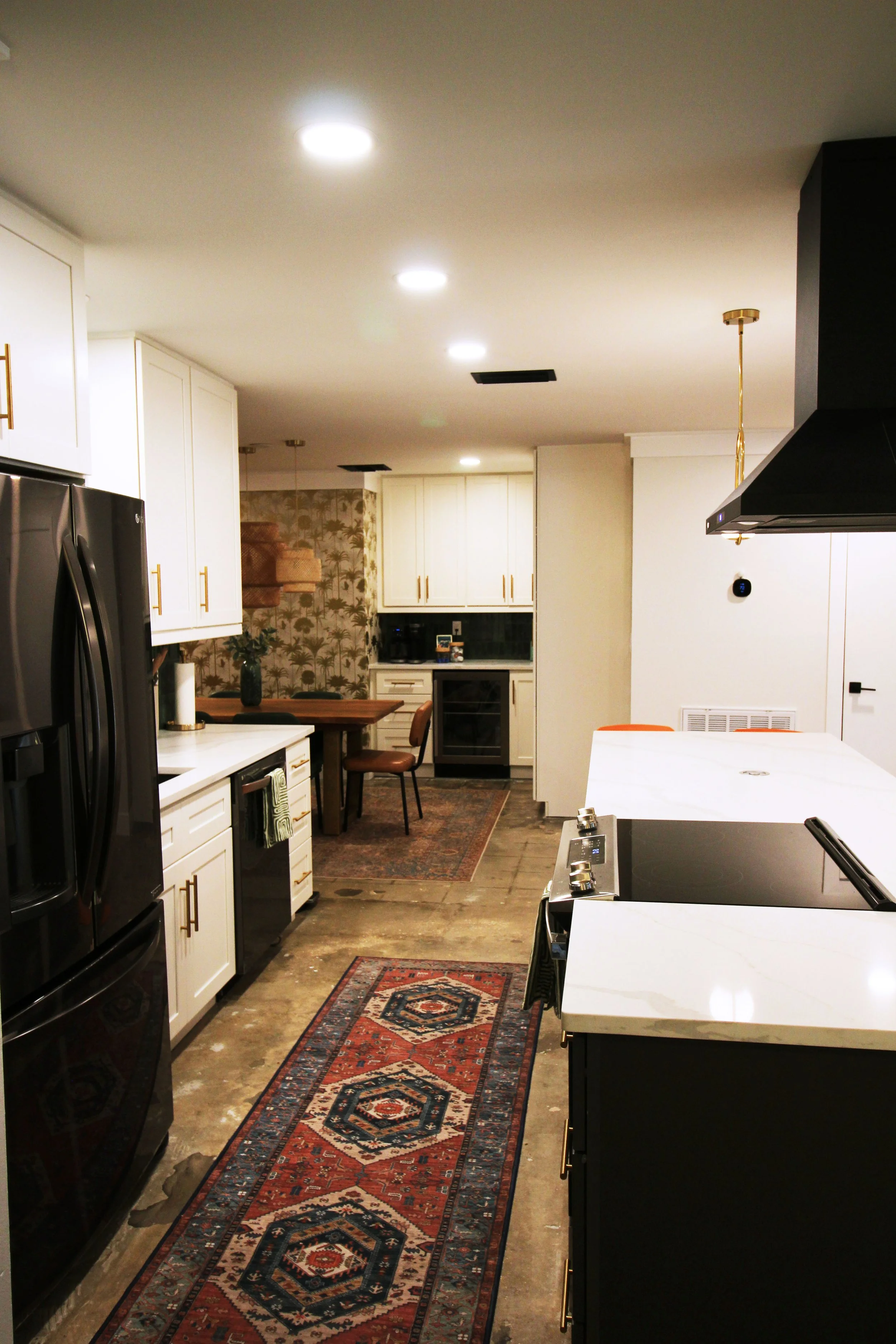 A modern kitchen with white shaker cabinets, black stainless steel appliances, a white quartz countertop, and a patterned runner rug on the floor.