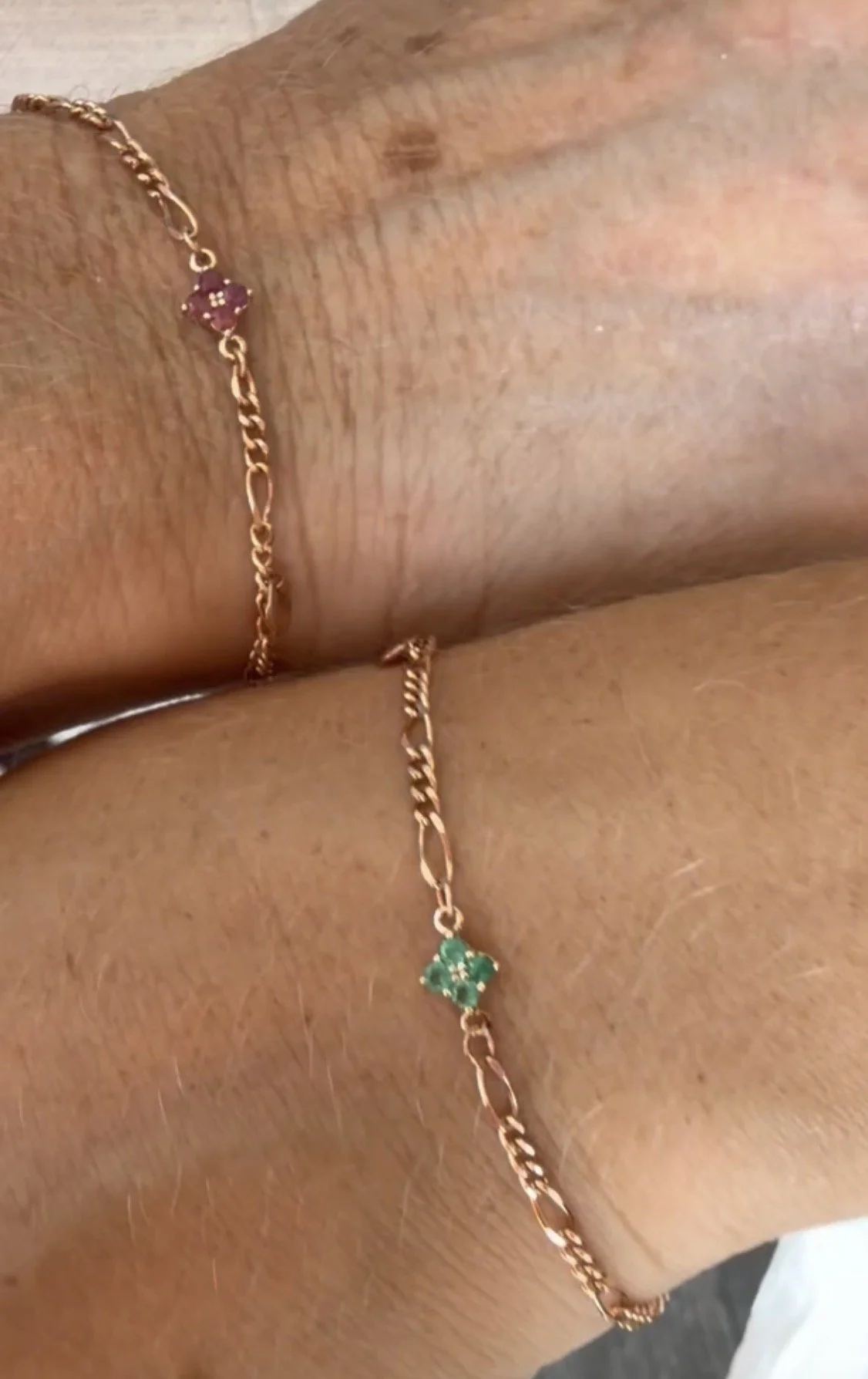 Multiple gold necklaces with charms, displayed on a beige heart-shaped jewelry holder, including a smiley face charm, a heart-shaped charm with a crystal, and a triple-heart cluster charm.