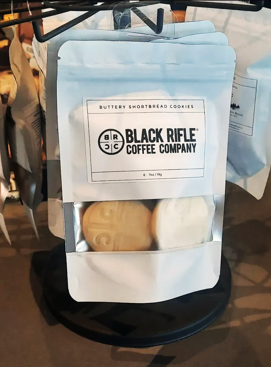 Bag of Buttery Shortbread Cookies from Black Rifle Coffee Company, visible through a clear window in the packaging, placed on a black surface.
