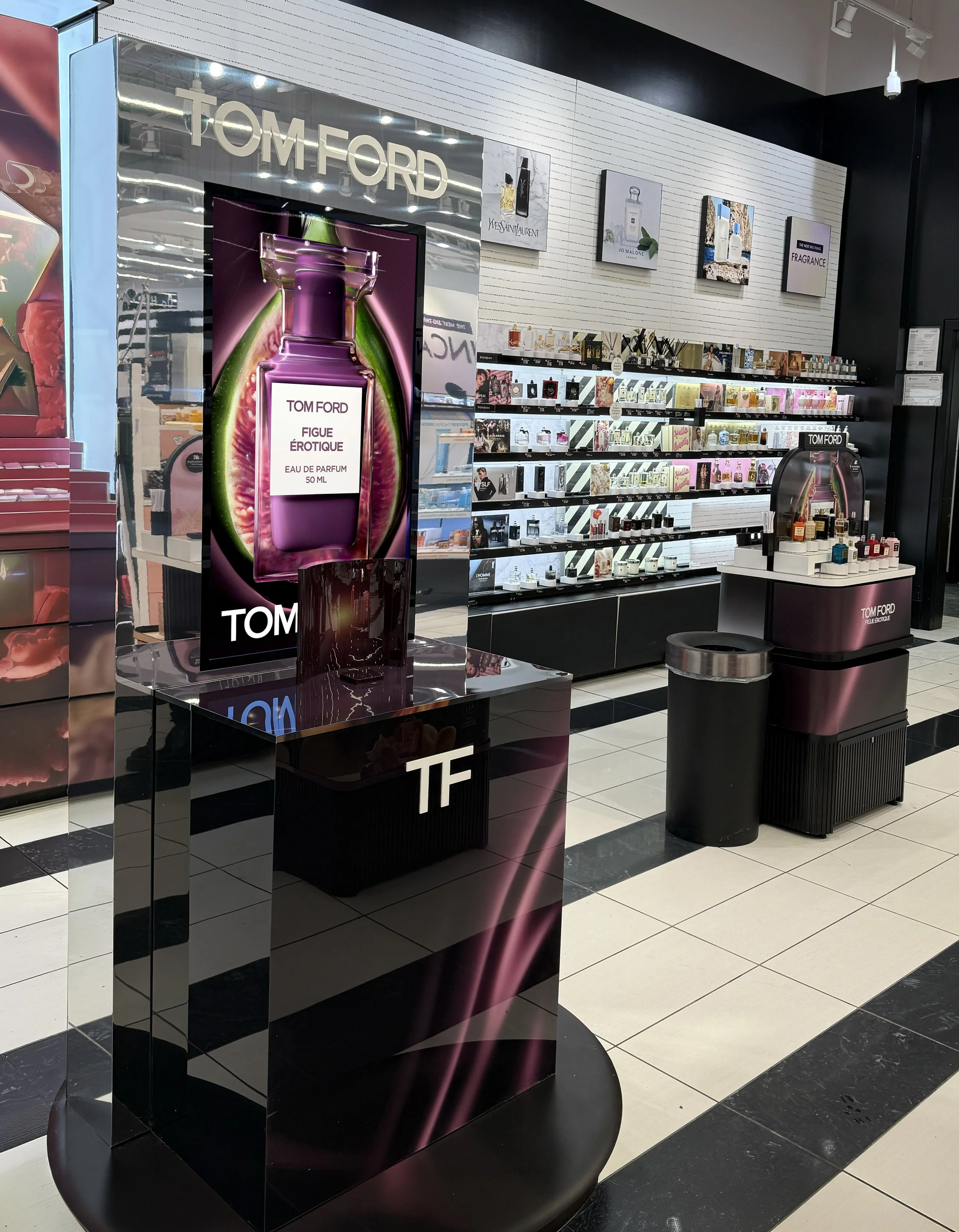 Display of Tom Ford fragrances in a retail store with a large digital advertisement showing a Tom Ford perfume bottle.
