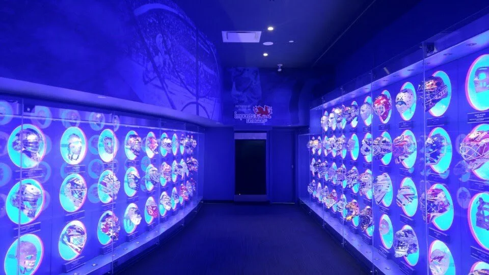 ~An indoor exhibit with illuminated display cases filled with model cars, backlit in blue, arranged on both sides of a walkway leading to a door.