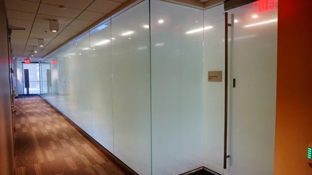 ~Empty hallway with glass walls and wooden flooring, with doors and lighting fixtures.
