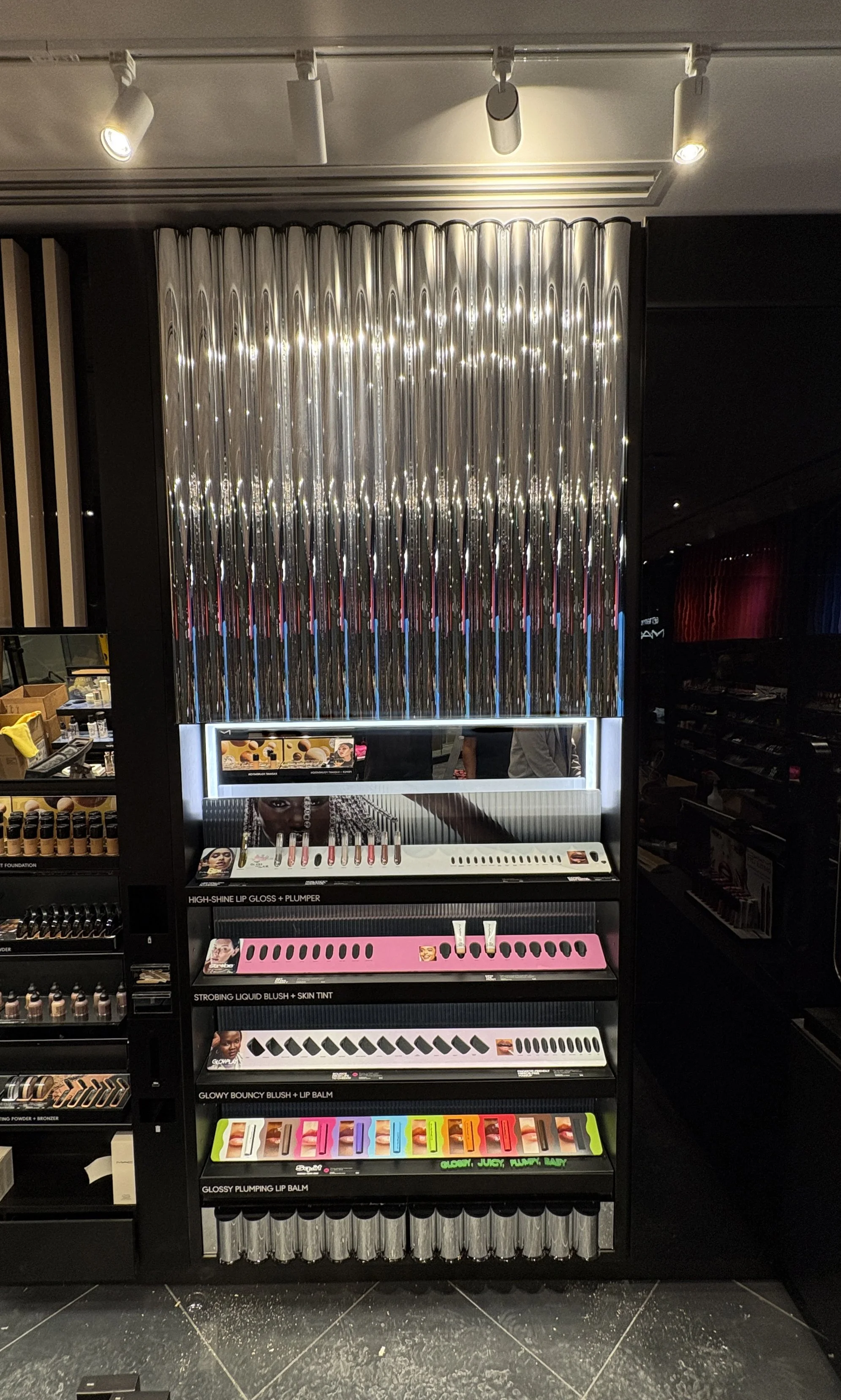 Display of makeup products including lip gloss, blush, and lip balm on black shelves in a cosmetic store.