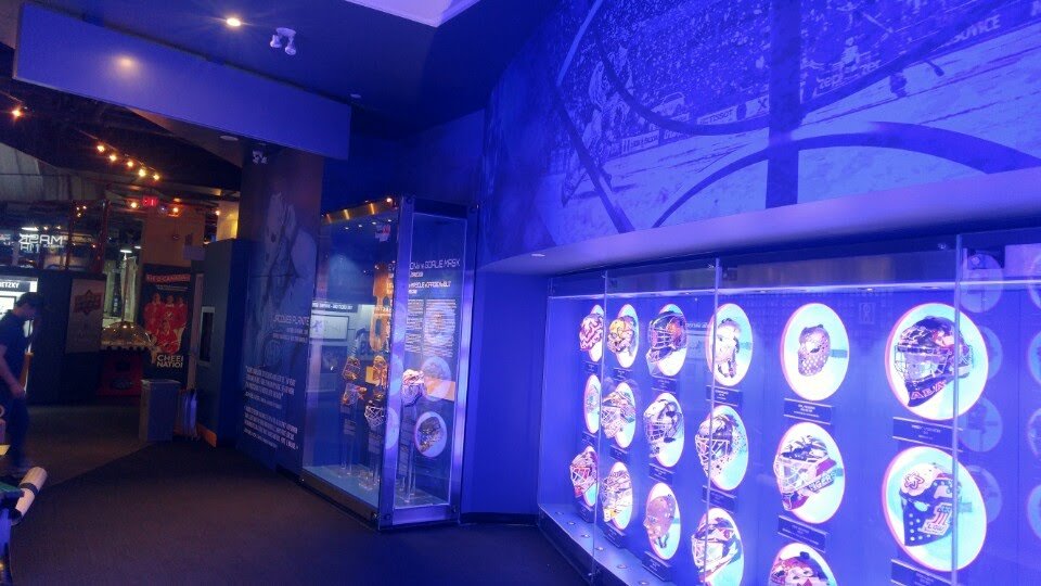 ~Display case with illuminated collectible pins or badges featuring various designs, set against a blue-lit museum or exhibit environment.