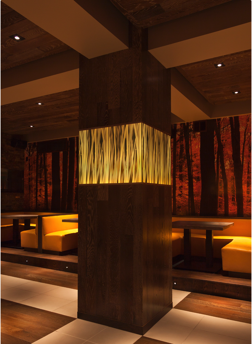 ~Interior of a restaurant with booth seating, wood accents, and a decorative illuminated wall feature with onyx or similar material, and a forest mural on the wall in the background.