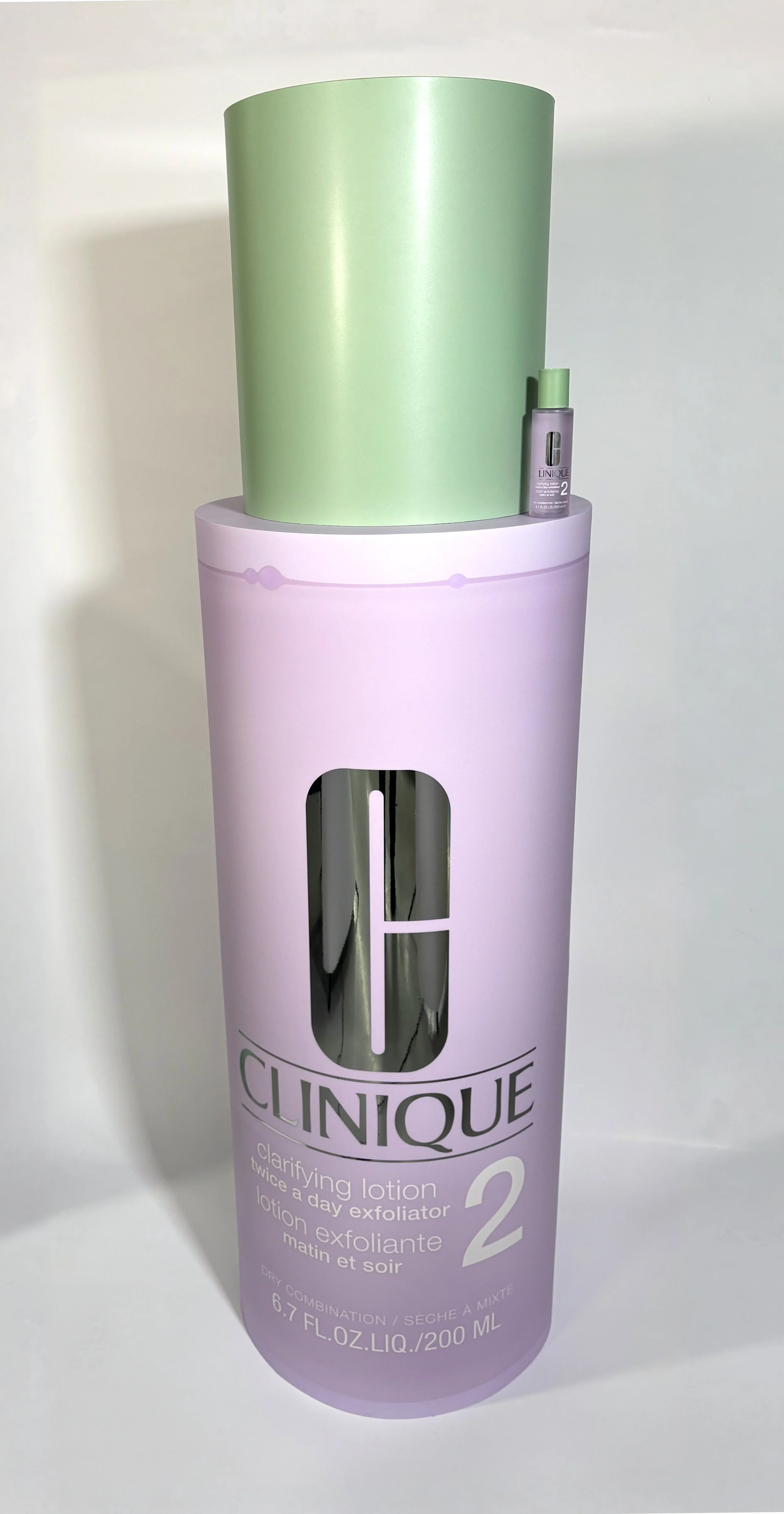 Oversize Clinique clarifying lotion bottle with a green cap on a pastel purple surface
