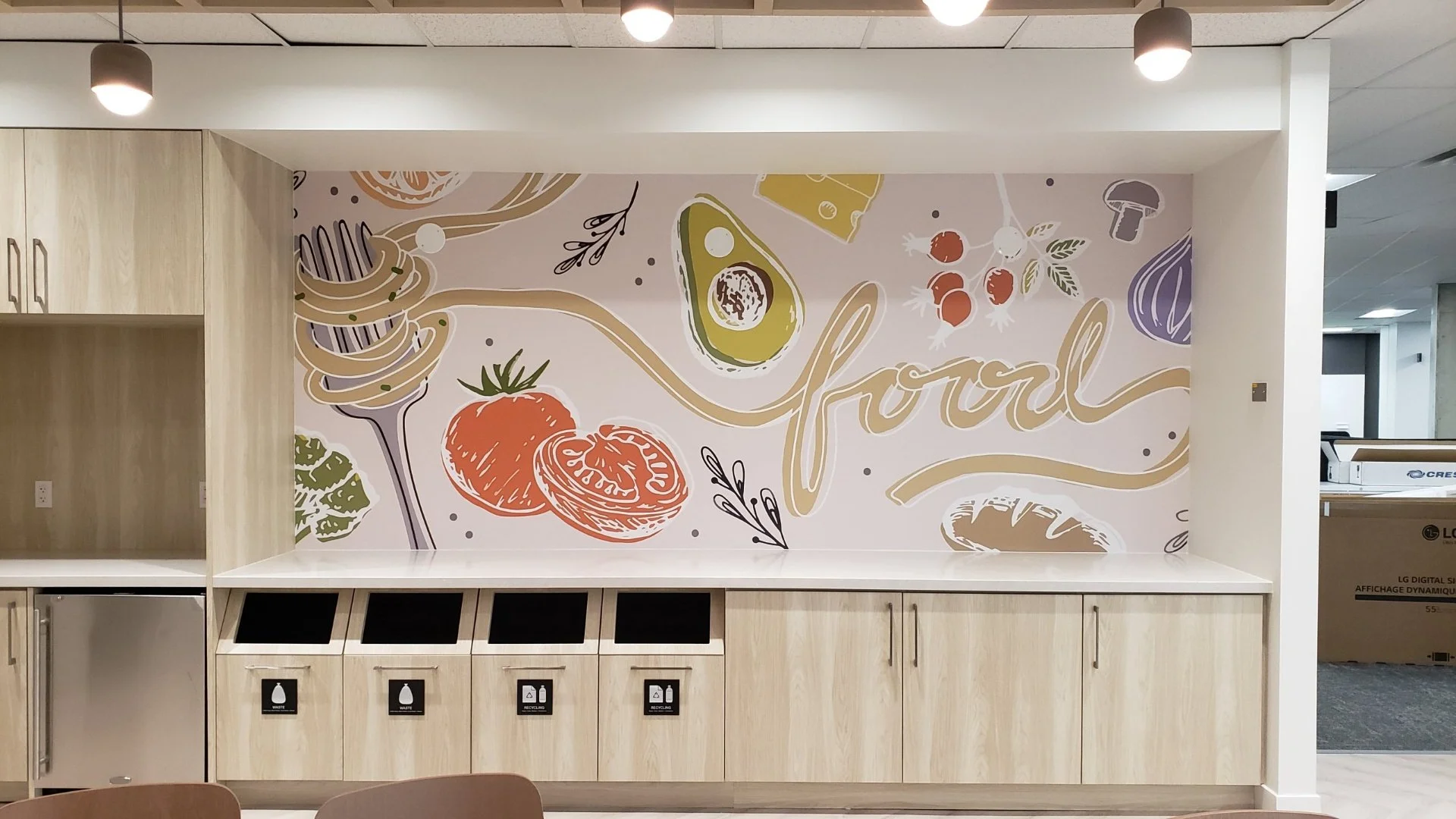 ~Decorative wall mural with illustrations of vegetables, herbs, and the word 'Yorbal' in calligraphy, above a counter with hygienic stations in a modern indoor setting.
