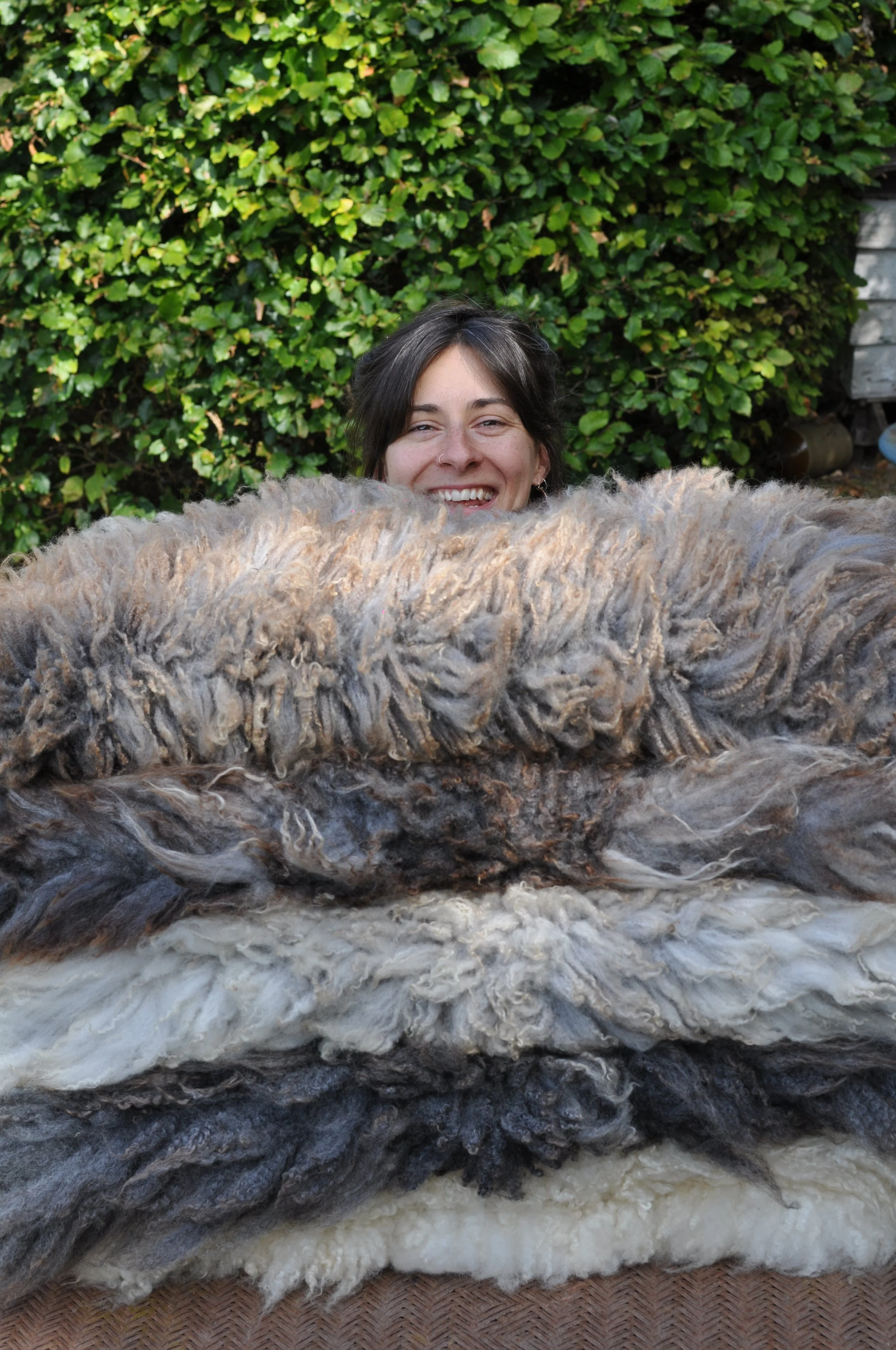 Steph from the Wild Plant Lab holding a stack of felted sheepskin rugs