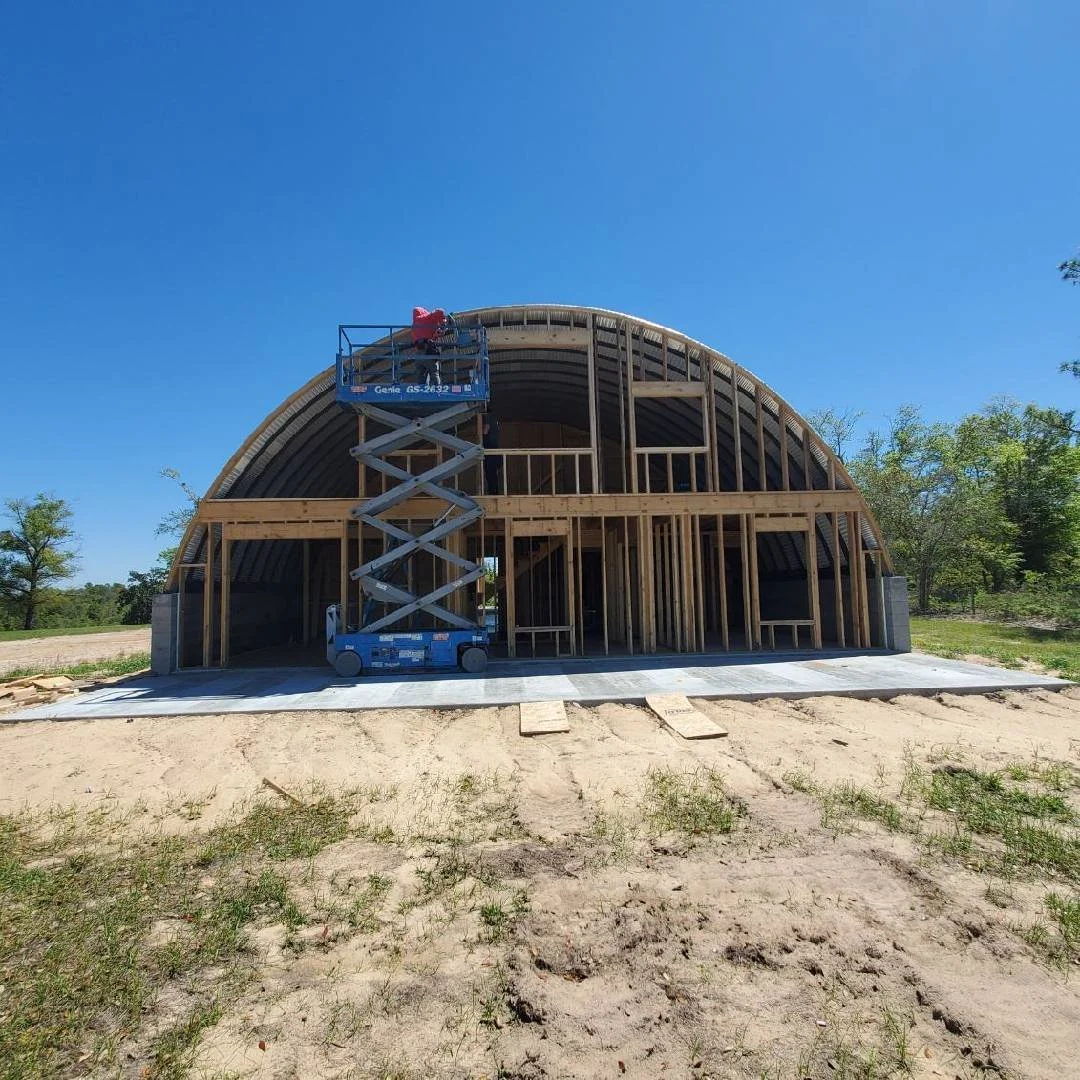 Curved wood building shell under construction with scaffolding and lift, showcasing custom structural framing by Tindall Construction.