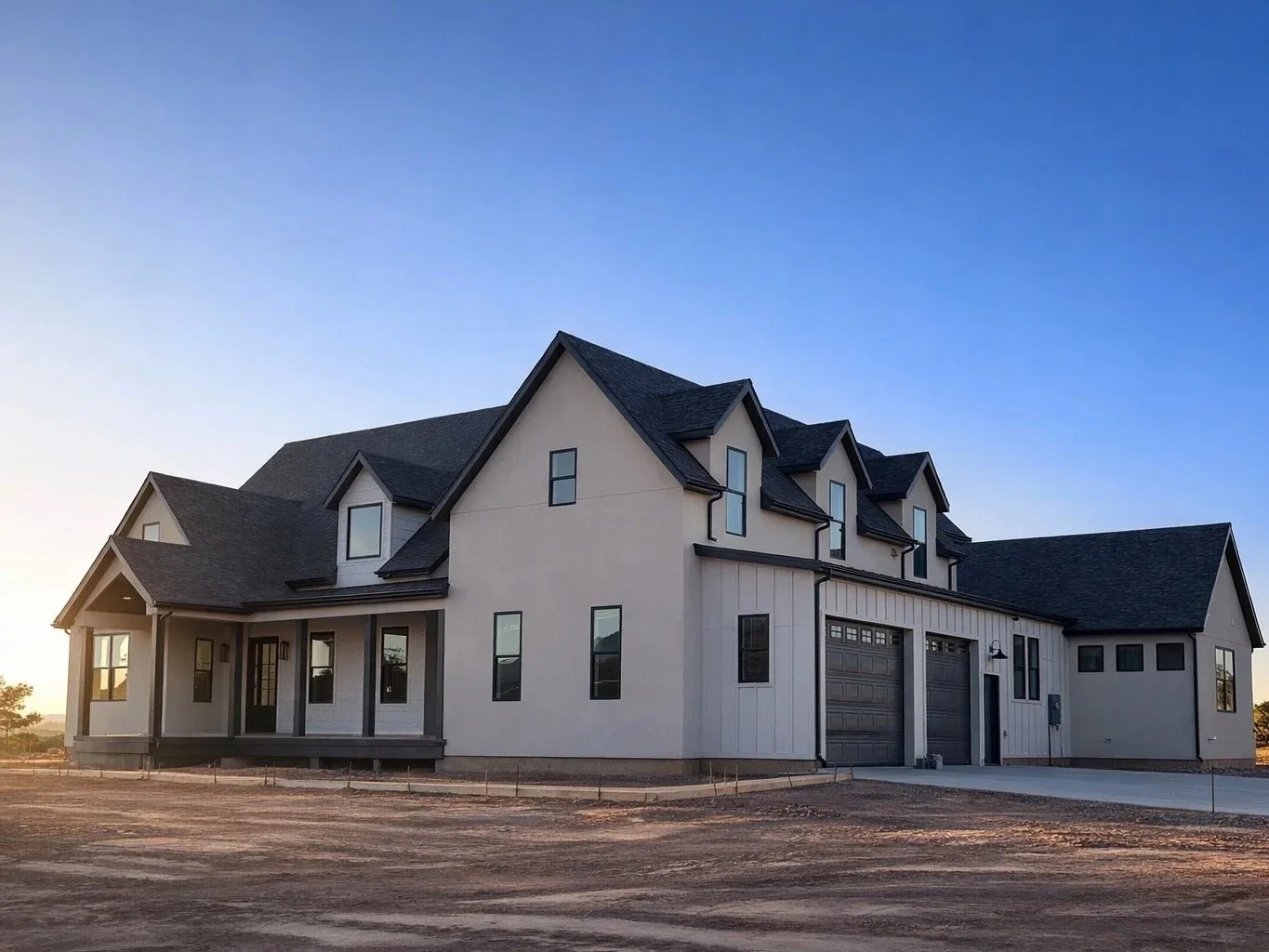 Modern white house with black roof and multiple gables, front porch, and attached garage, set against a blue sky.
