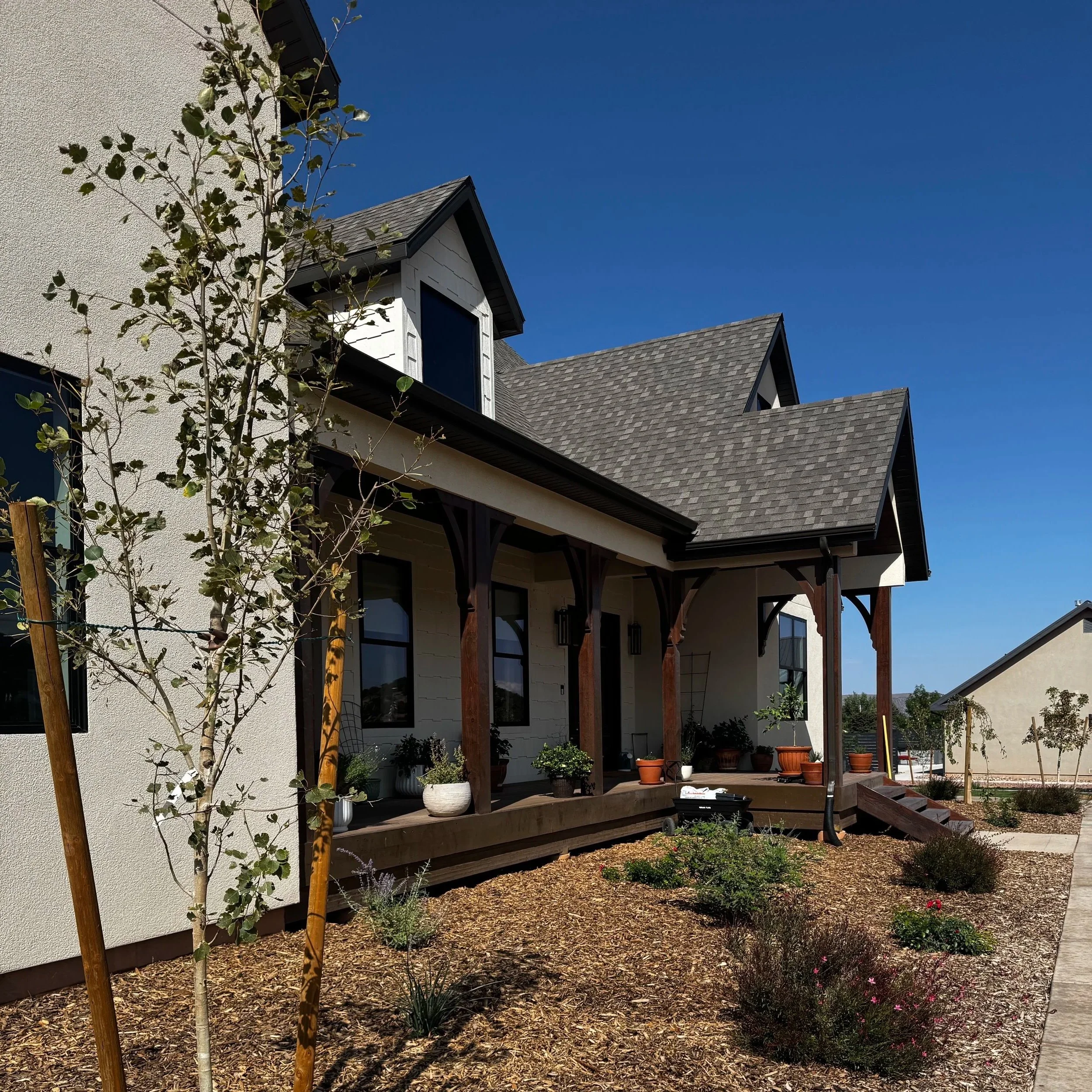 A modern house with large windows, surrounded by blooming purple and pink hydrangea flowers and small garden lights, set against a hilly green landscape under a cloudy sky.