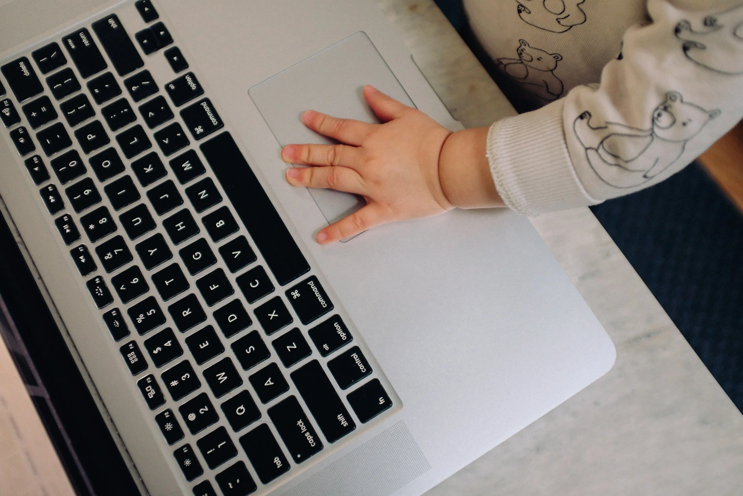 Close-up of a person's hand resting on a silver laptop keyboard, wearing a sleeve with bear illustrations.