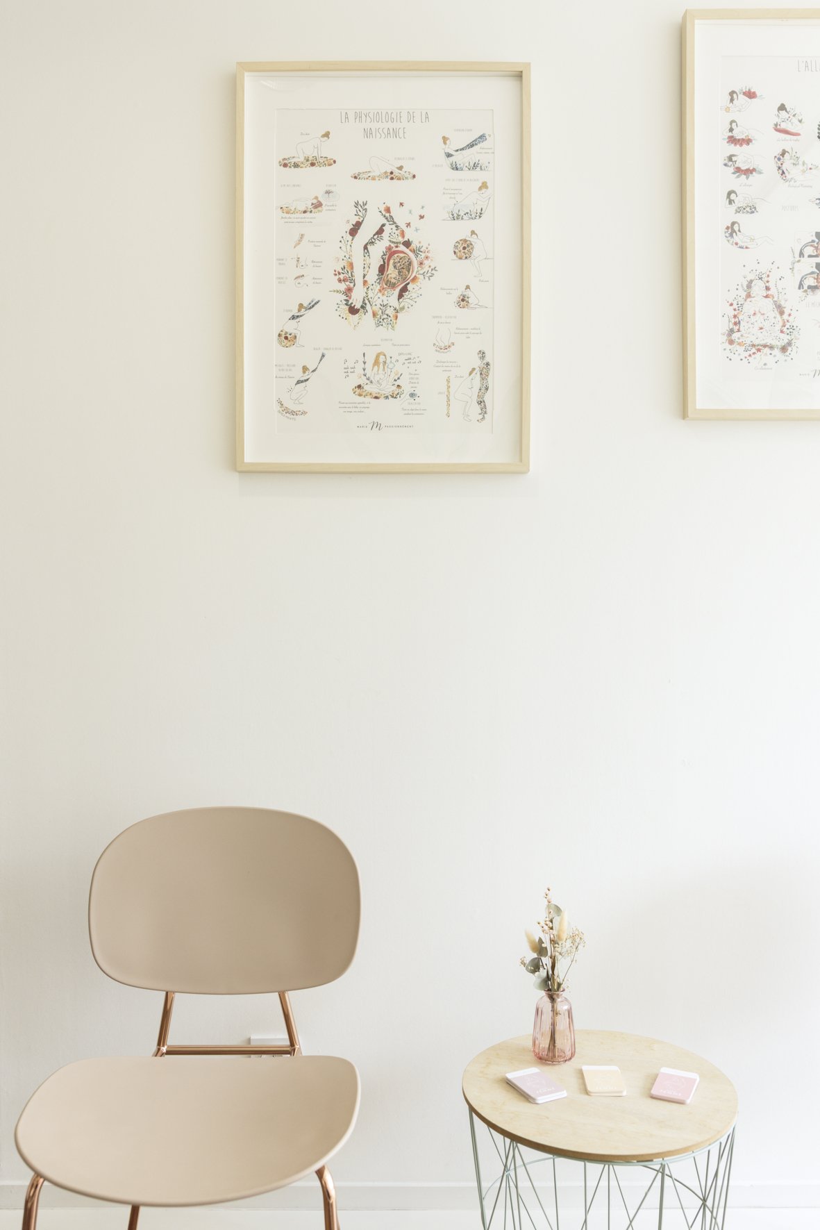 Intérieur minimaliste avec une chaise beige, une petite table ronde en marbre avec un vase de fleurs, et deux cadres avec des illustrations dans un mur blanc. Salle d'attente du Cabinet de Sage-Femme Chalotais à Rennes Cesson-Sévigné. Grossesse