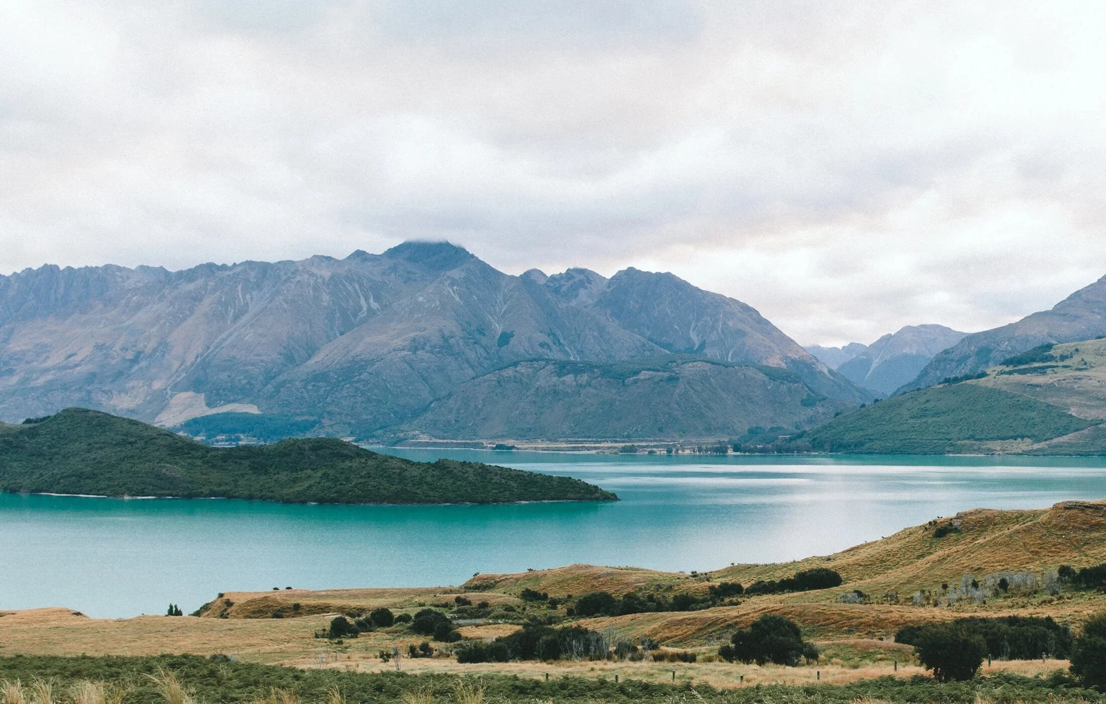 Scenic view of a large body of water with green hills and mountains in the background under a cloudy sky.