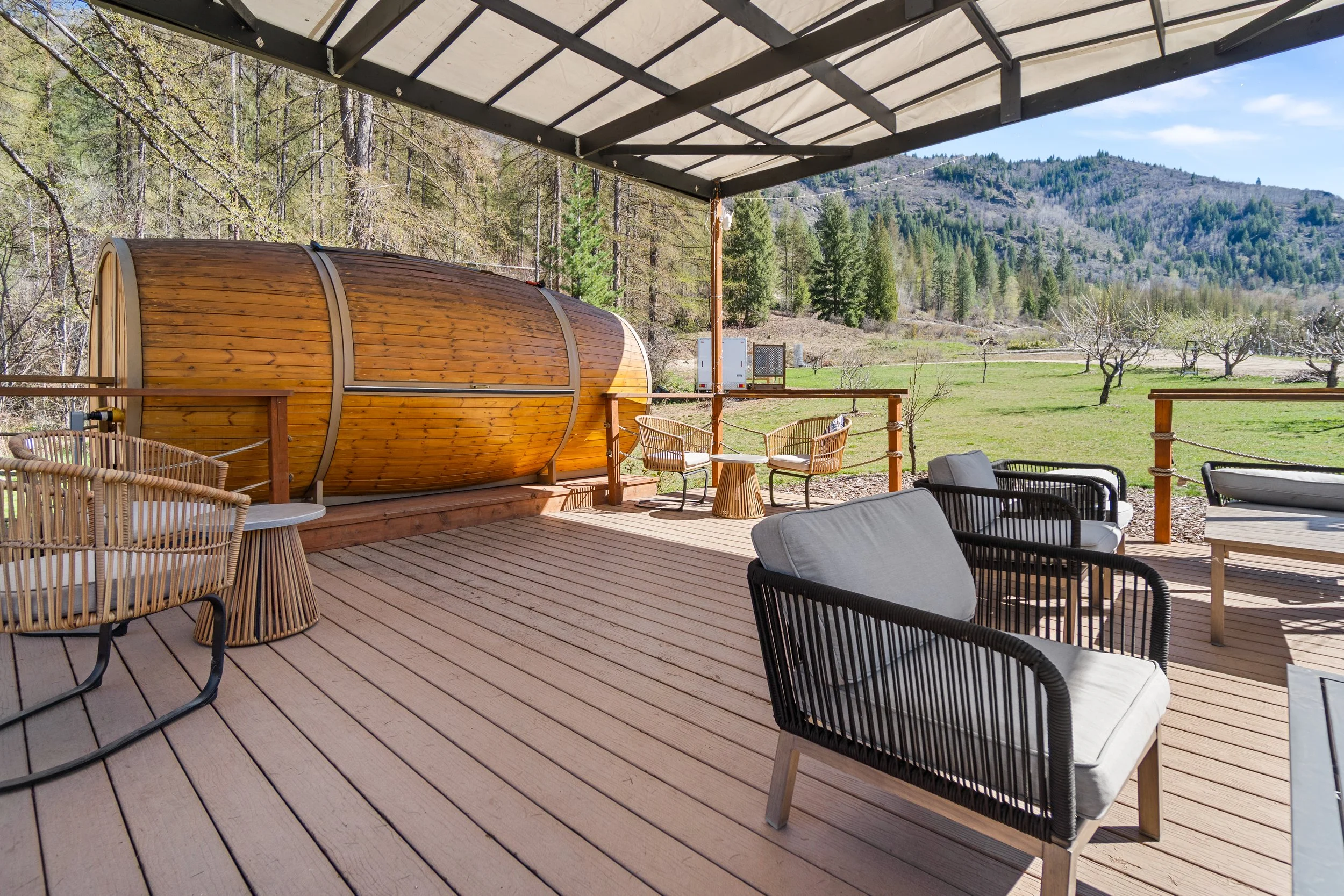 spacious outdoor Wine Tasting deck with modern outdoor furniture, including cushioned chairs and small tables, overlooking a green yard with trees and mountains in the distance. Taken at Mountain Soul Wines in Trail BC