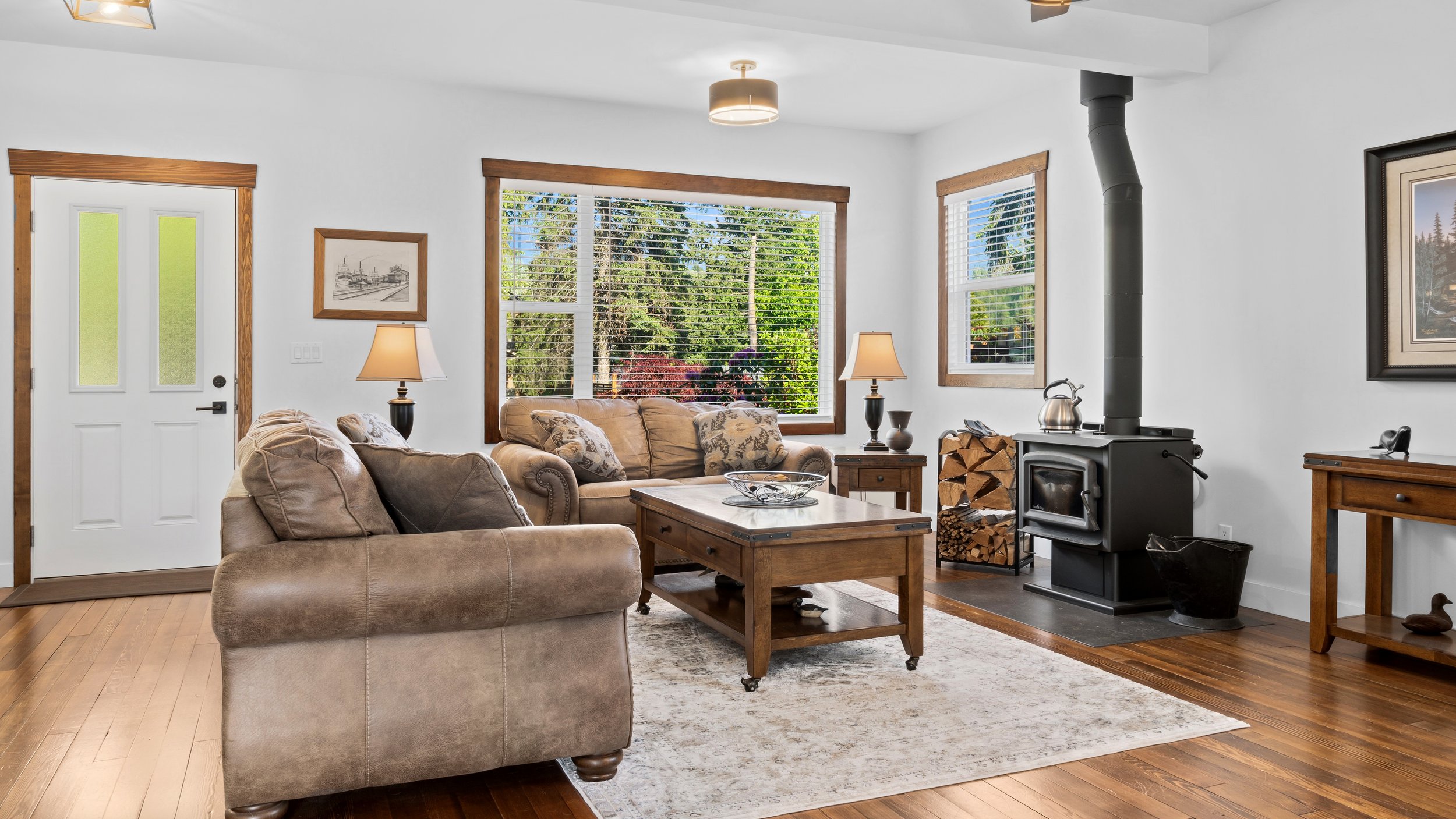 Living room with beige sofas, wooden furniture, large windows with blinds, a wood stove, and decorative lamps.