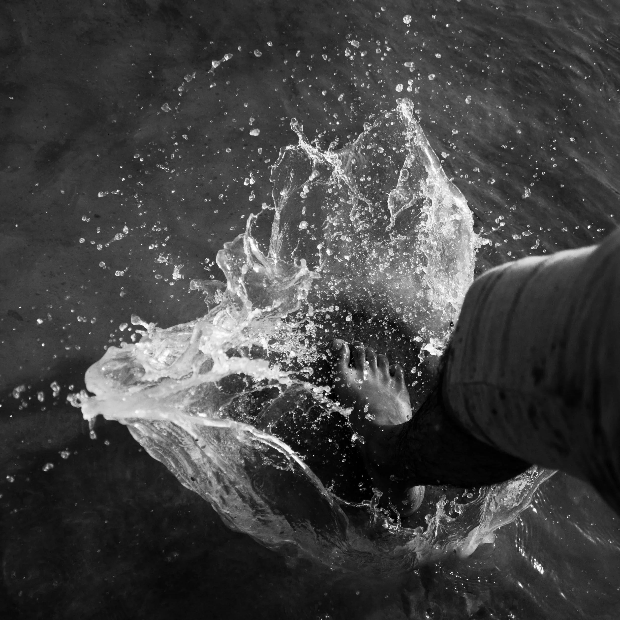 Photograph of a barefoot foot splashing forcefully into water, evoking vitality, sensation, emotional intensity, embodiment, and the nervous system’s relationship to aliveness.
