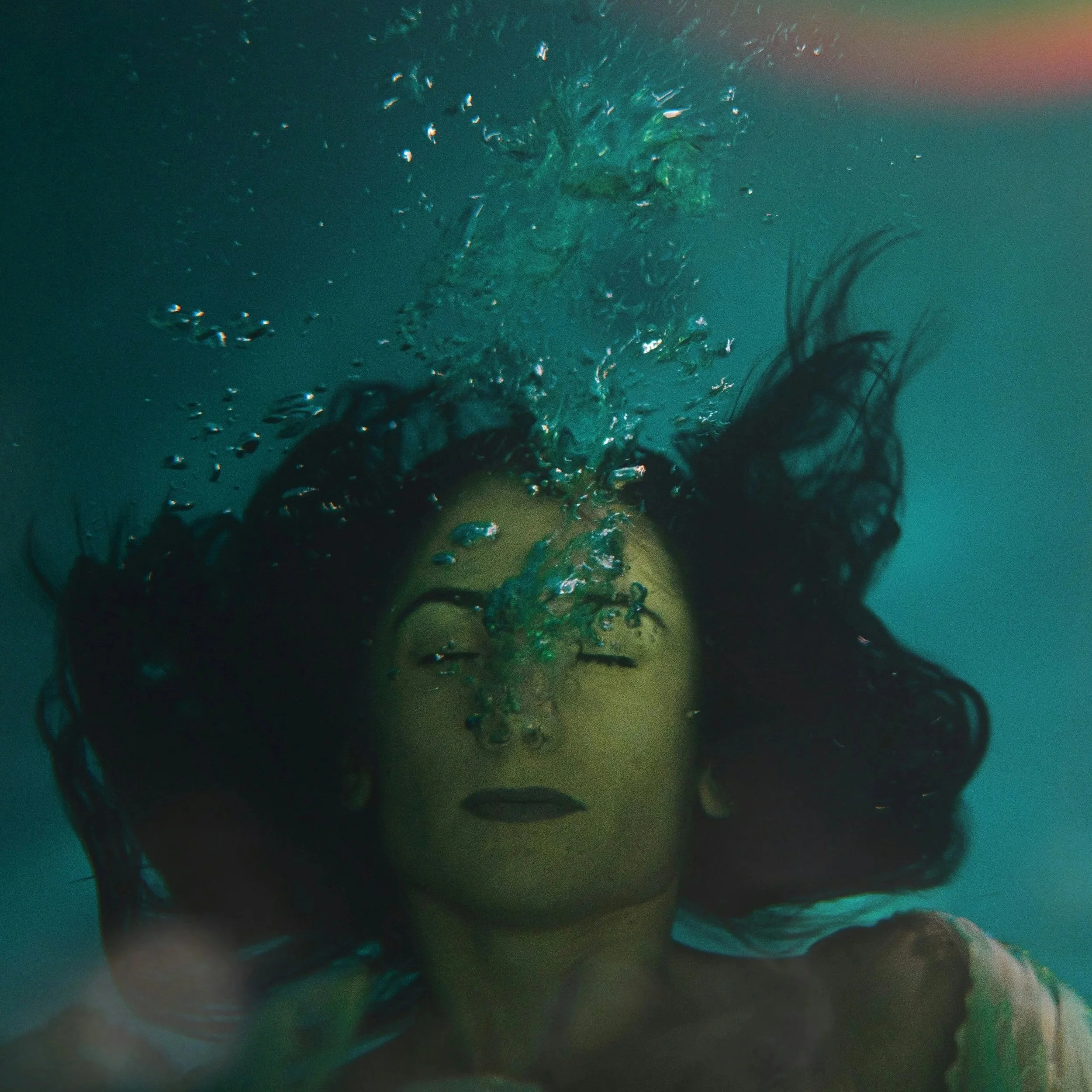 Underwater portrait of a woman holding her breath with bubbles rising around her, symbolizing emotional regulation, nervous system overwhelm, vulnerability, healing, and learning to tolerate joy and aliveness.