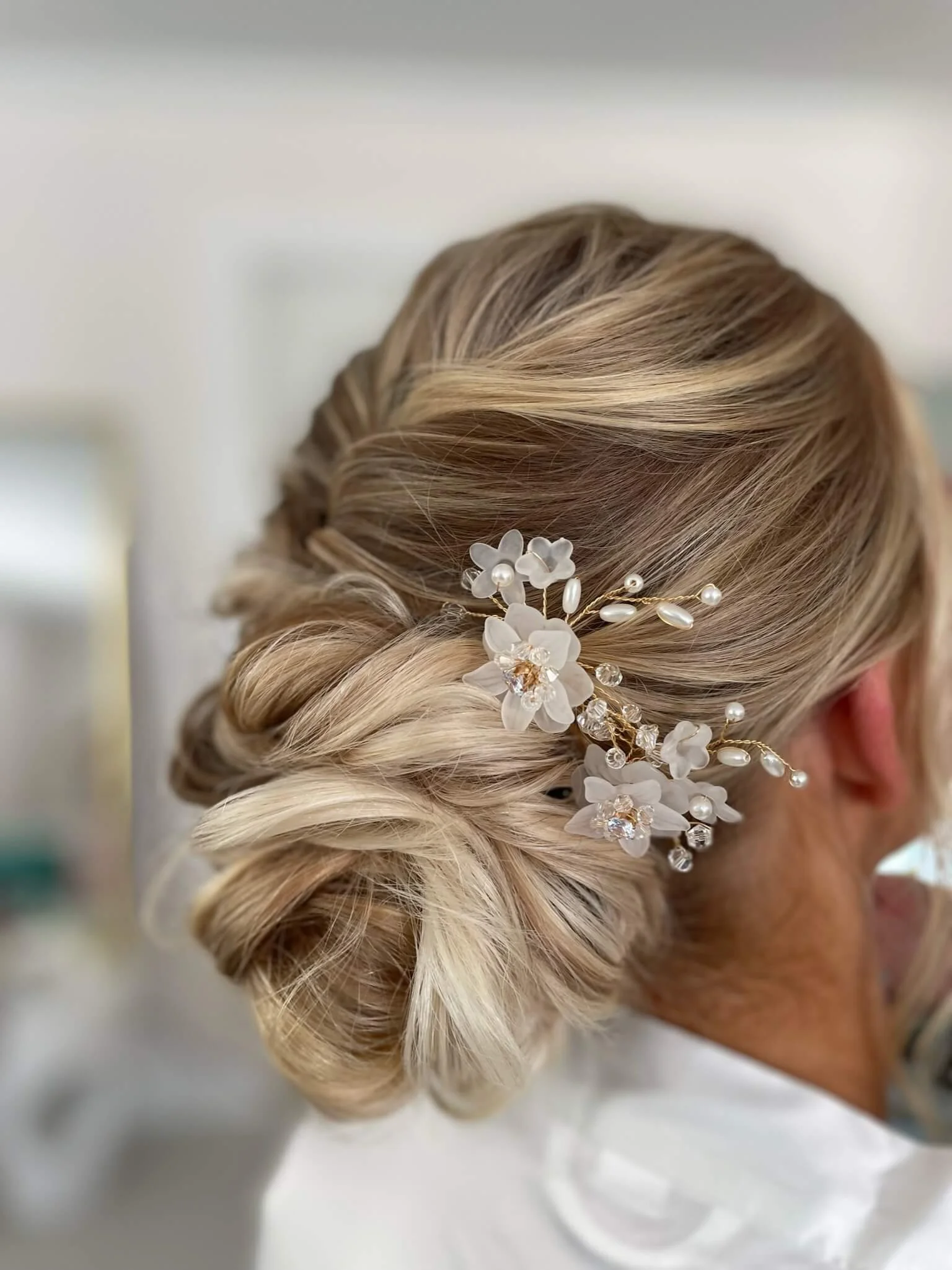 Elegant blonde hair styled in an updo with a white floral hair accessory with pearls and crystals.