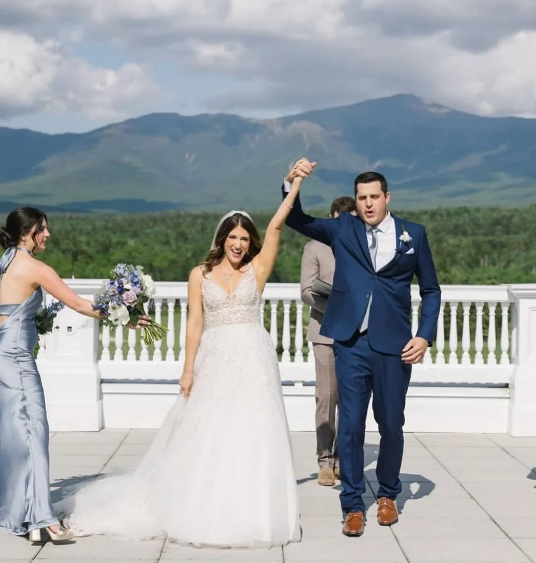 A bride and groom holding hands and celebrating outdoors with mountains in the background, during their wedding ceremony.